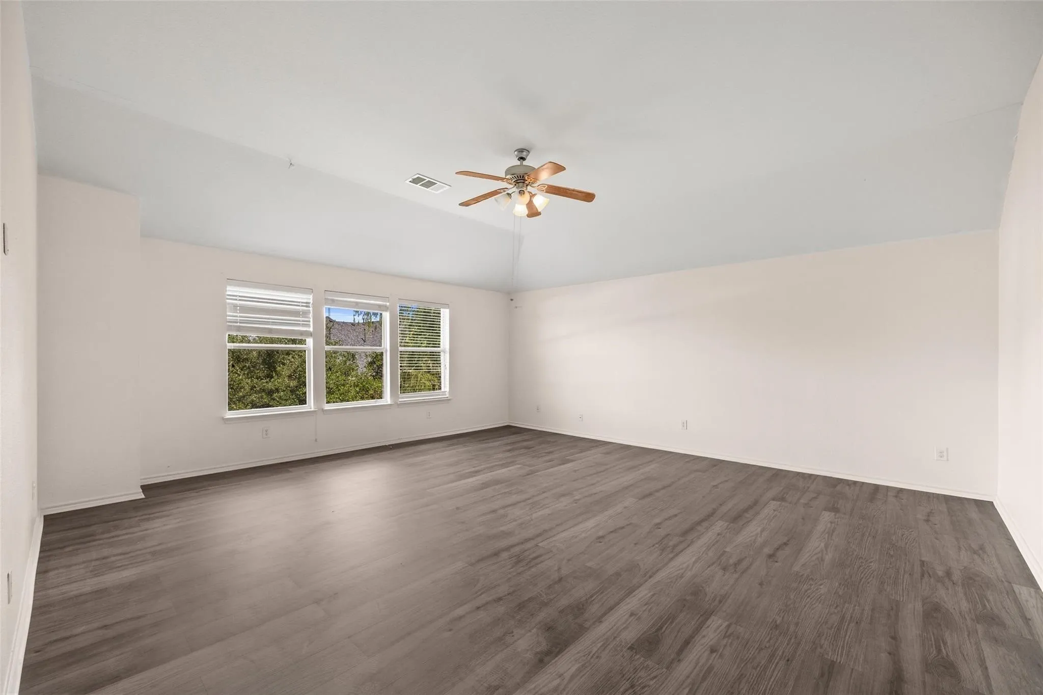 Spacious room featuring wood-finish flooring, multiple windows, a ceiling fan, and vaulted ceilings