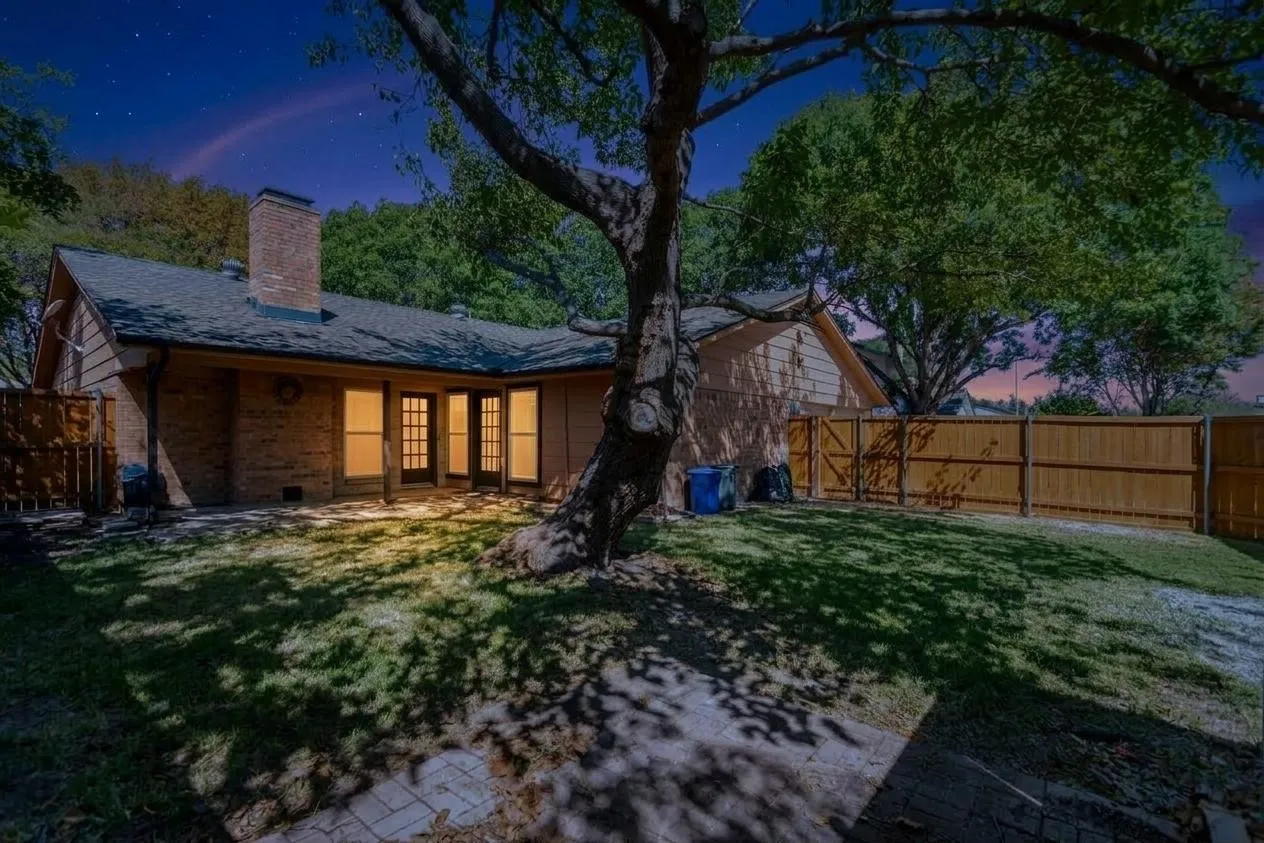 Expansive backyard featuring a mature shade tree, brick exterior, multi-pane glass doors, a brick chimney, and a wood privacy fence