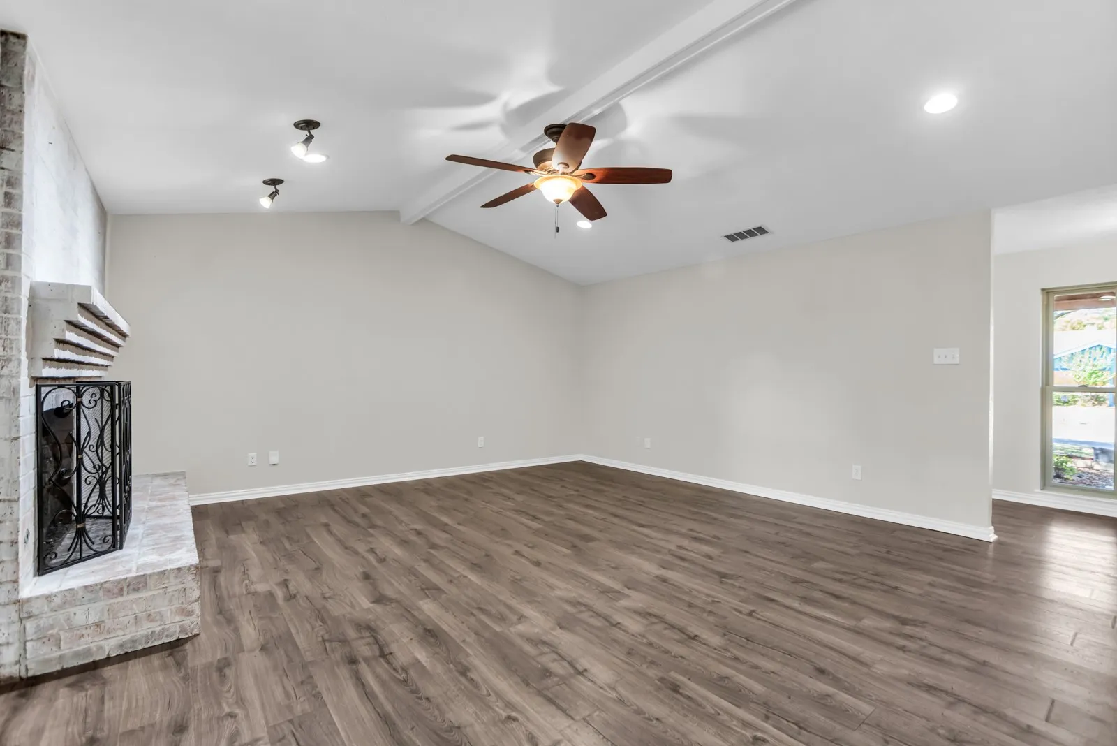 Vaulted ceiling with exposed beam, wood-finish flooring, brick fireplace with mantel, ceiling fan, and recessed lighting