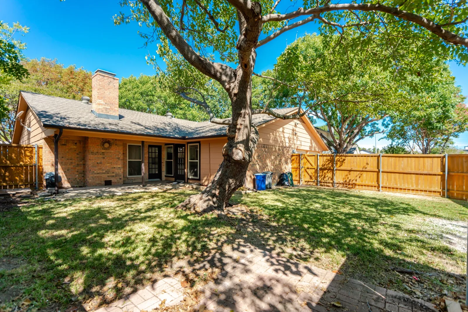 Expansive backyard featuring a manicured lawn, mature trees, brick patio, privacy fencing, and a brick exterior