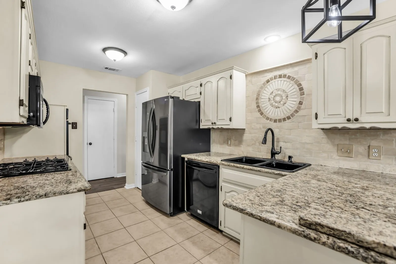 Kitchen featuring granite countertops, tile flooring, white cabinetry, a tile backsplash with a mosaic detail, and a black double basin sink with a gooseneck faucet