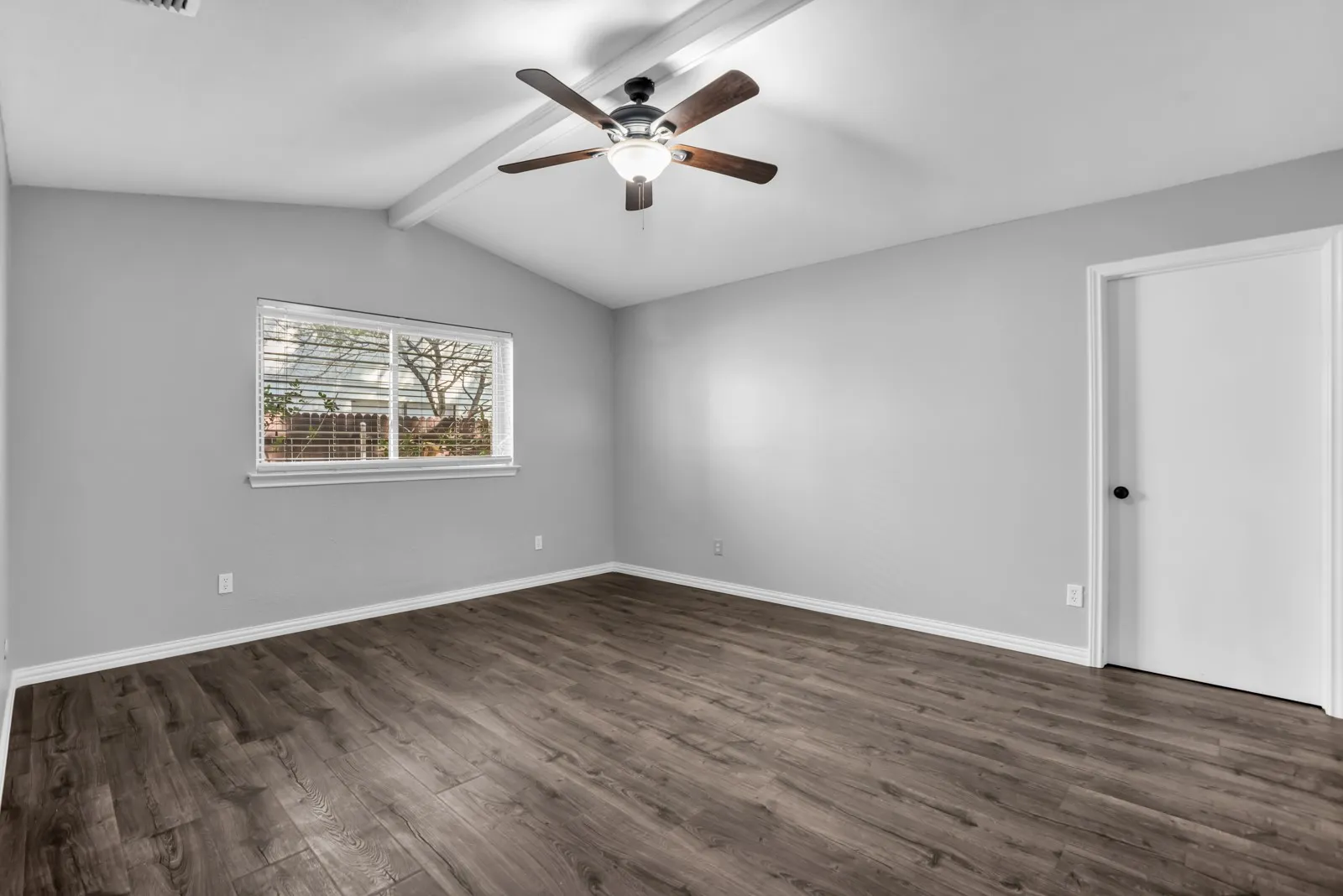 Vaulted ceiling featuring exposed beams, wood-finish flooring, a ceiling fan with integrated lighting, and a window with horizontal blinds