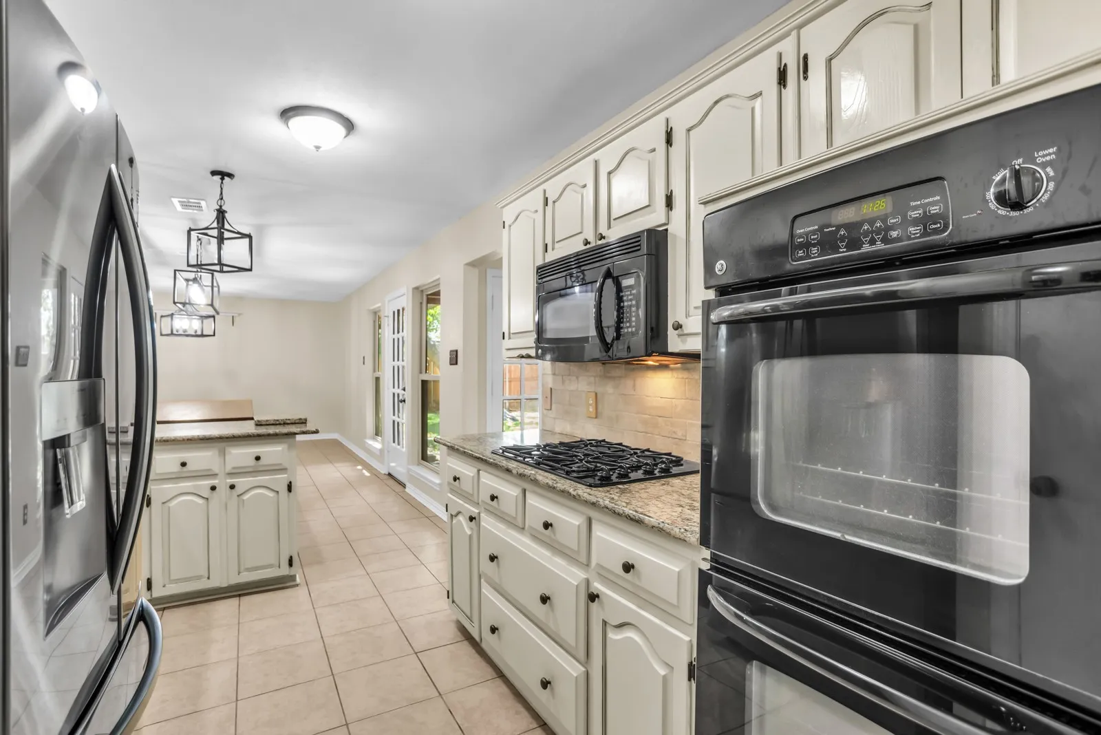 Kitchen featuring built-in double ovens, stainless steel refrigerator, tile flooring, granite countertops, and white cabinetry