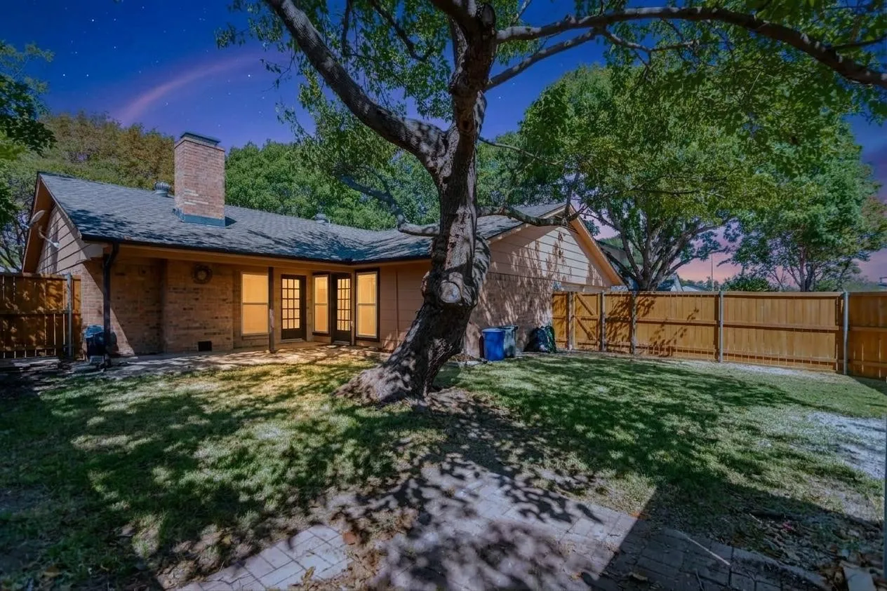 Expansive backyard featuring a mature tree, privacy fencing, brick patio, and multiple French doors