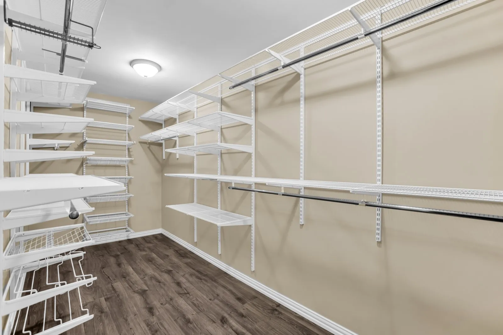 Walk-in closet featuring wood-finish flooring, white wire shelving, multiple hanging rods, and a ceiling-mounted light fixture