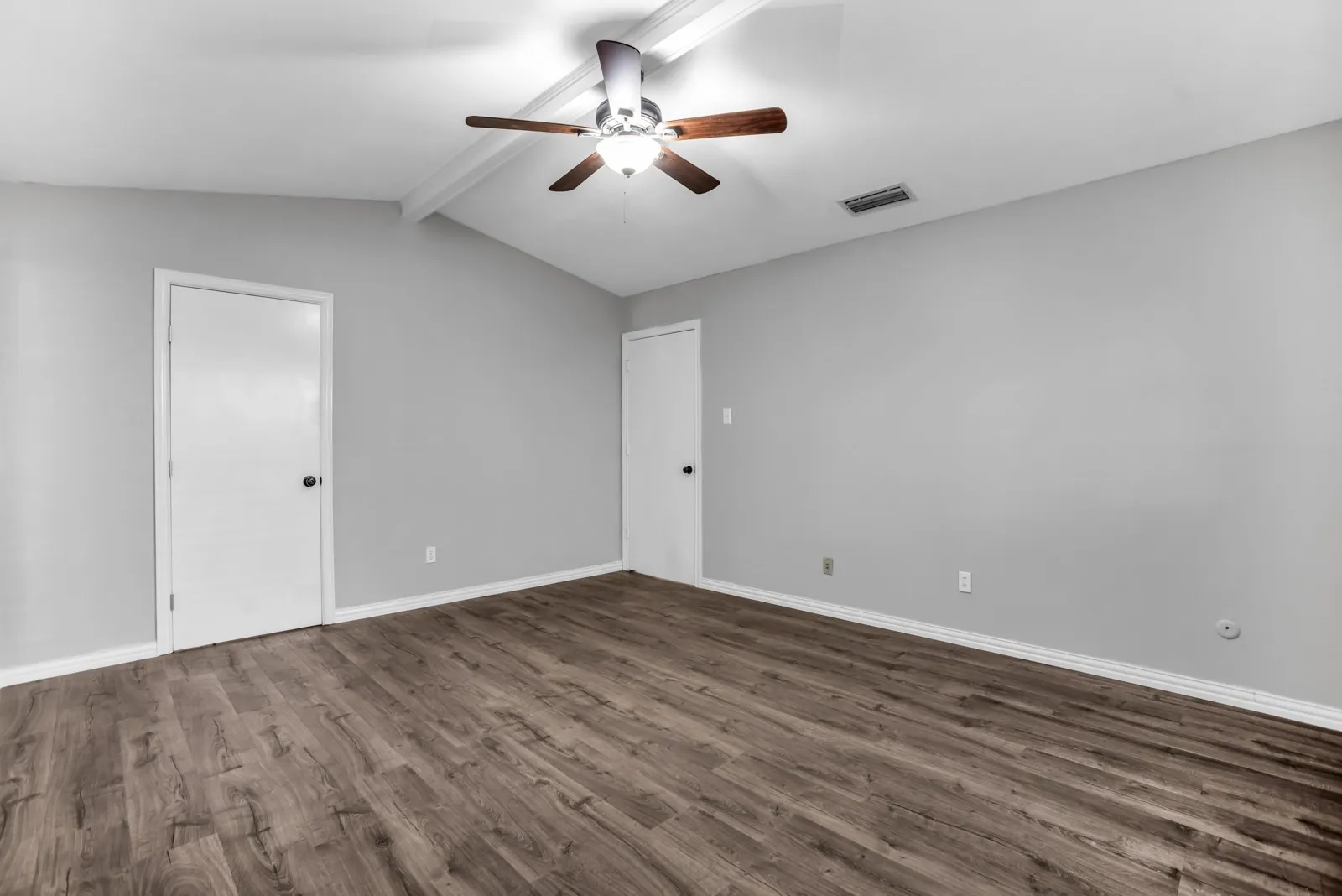 Vaulted ceiling with exposed beams, wood-finish flooring, and a ceiling fan with integrated lighting