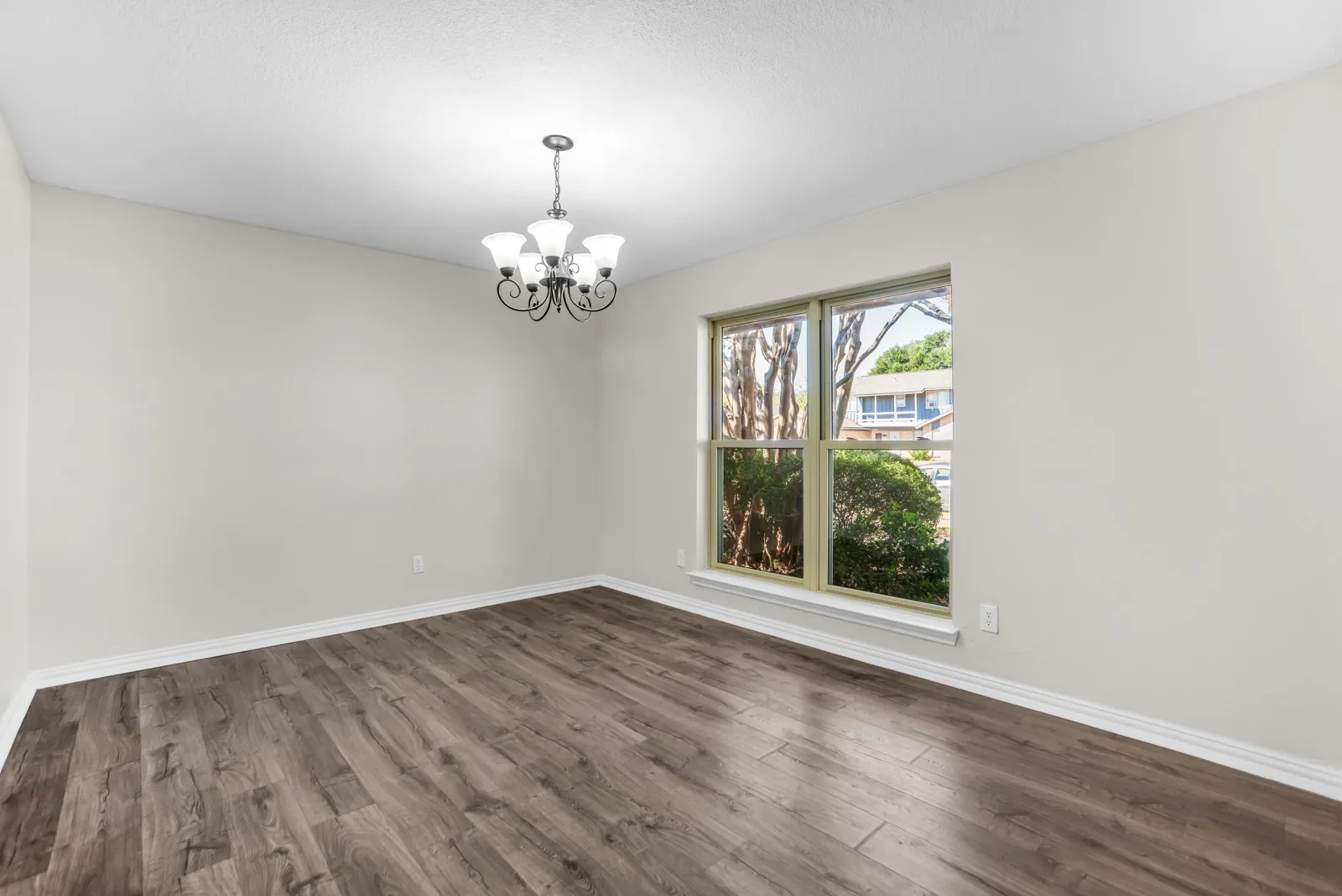 Spacious room featuring wood-finish flooring, a multi-pane window, and a five-light chandelier