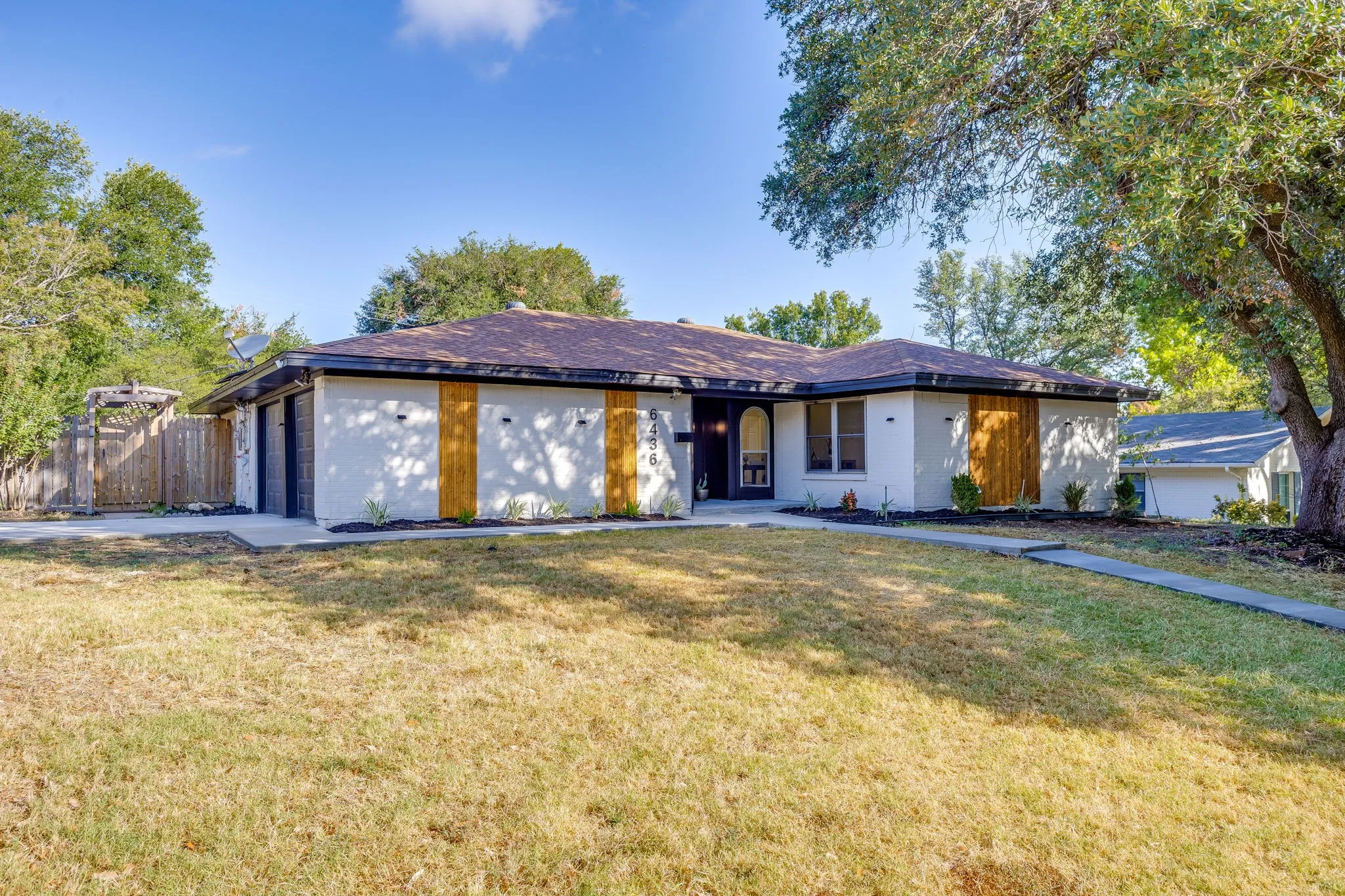 Single-story residence featuring a white stucco exterior with vertical wood accents and a dark roof