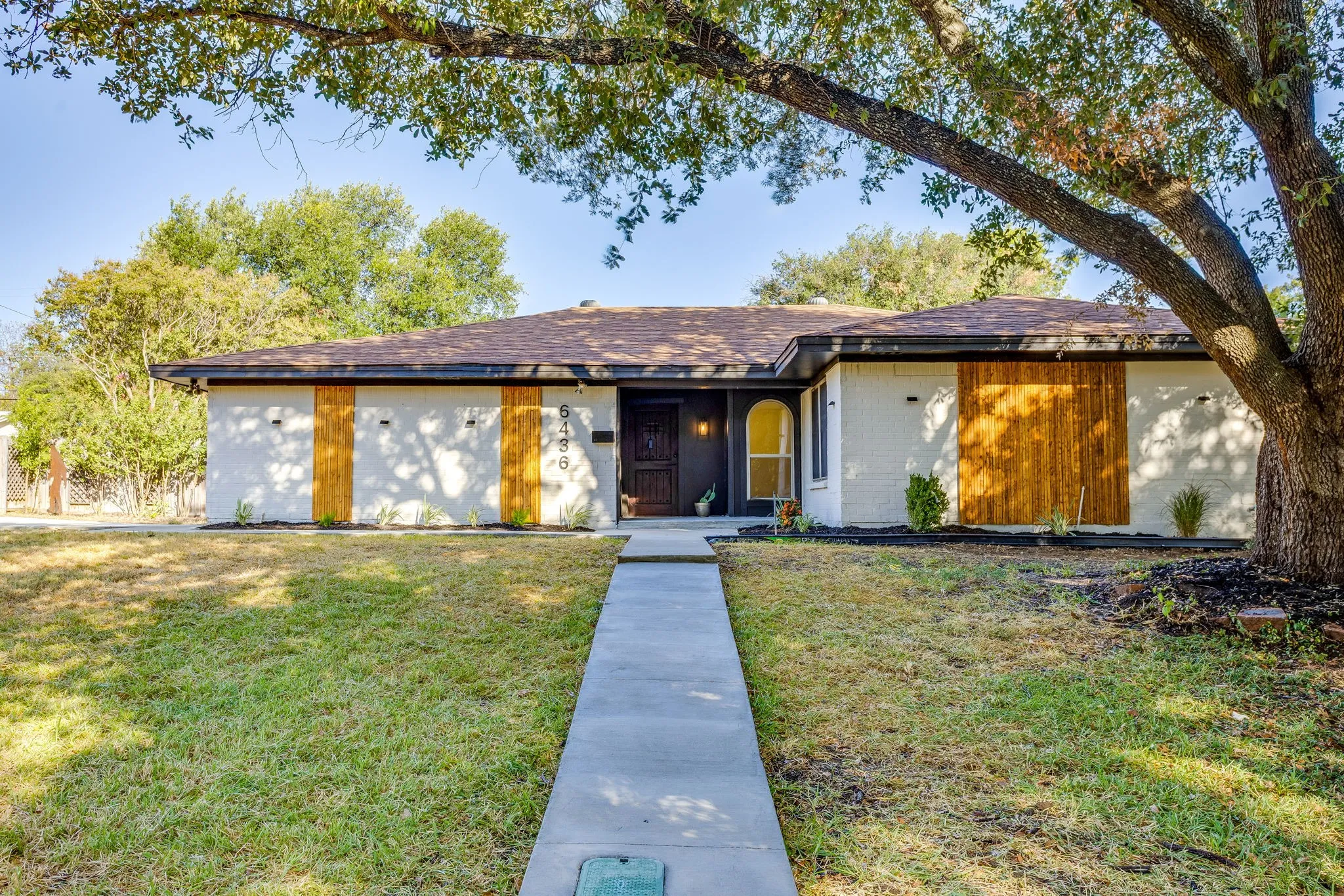 Single-story residence featuring a white painted brick exterior, wood-paneled accents, and a dark-toned front entry with an arched window