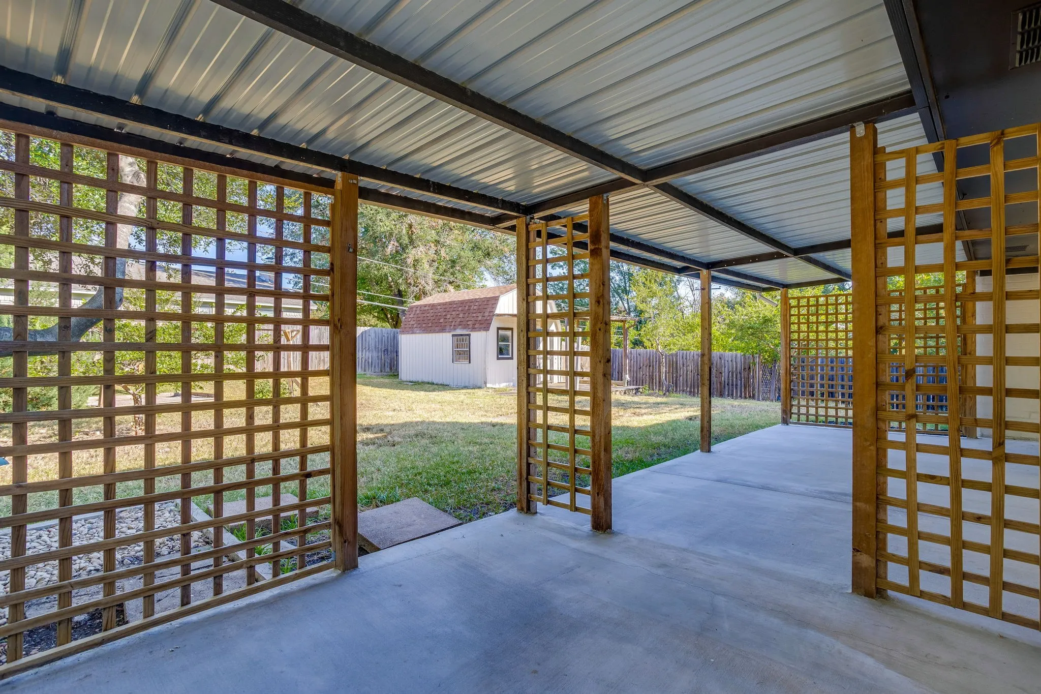 Covered patio with a corrugated metal roof, concrete flooring, and decorative wooden lattice screens