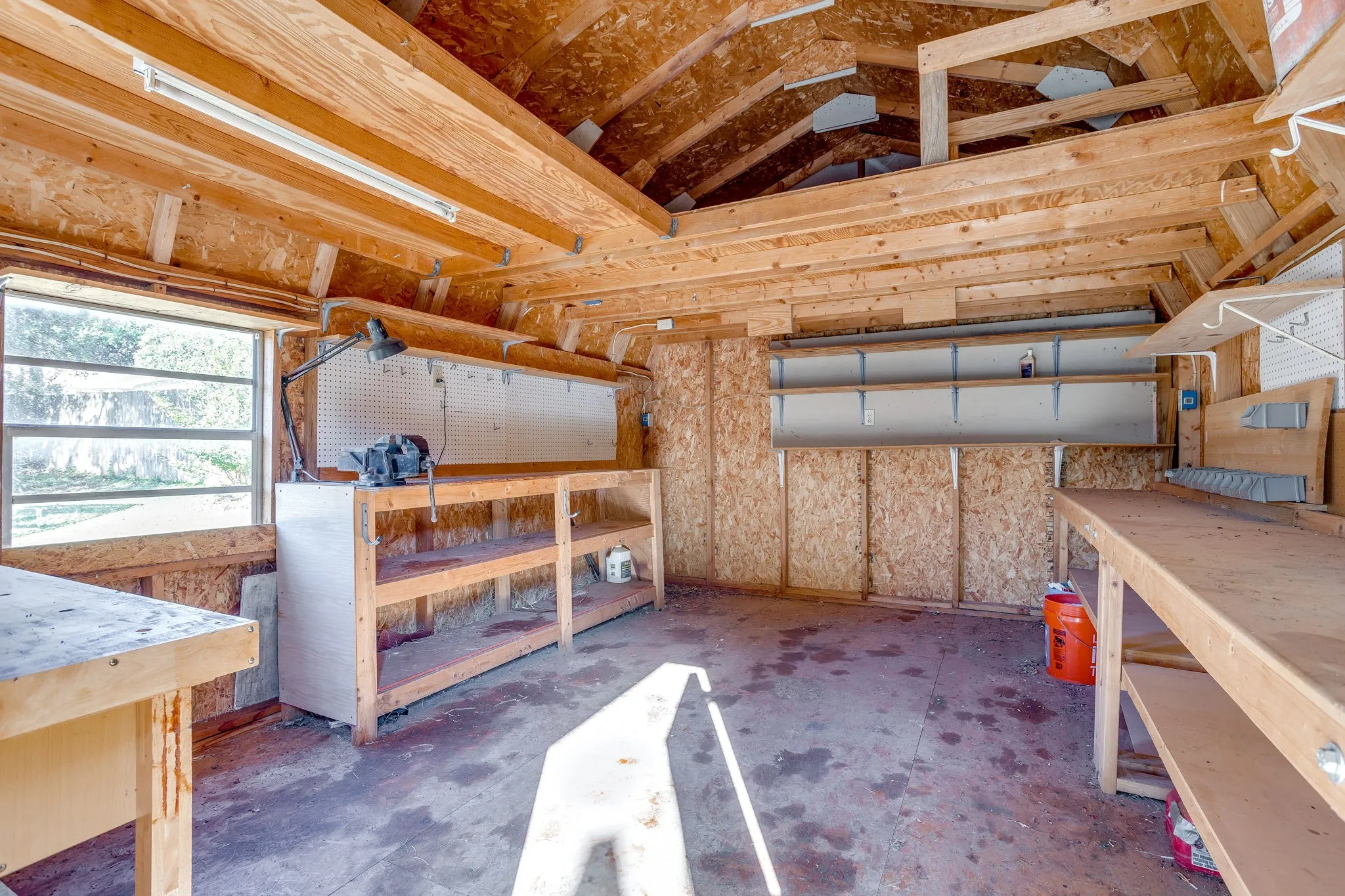 Work shed featuring exposed wood beam construction, integrated shelving, a workbench, and a window