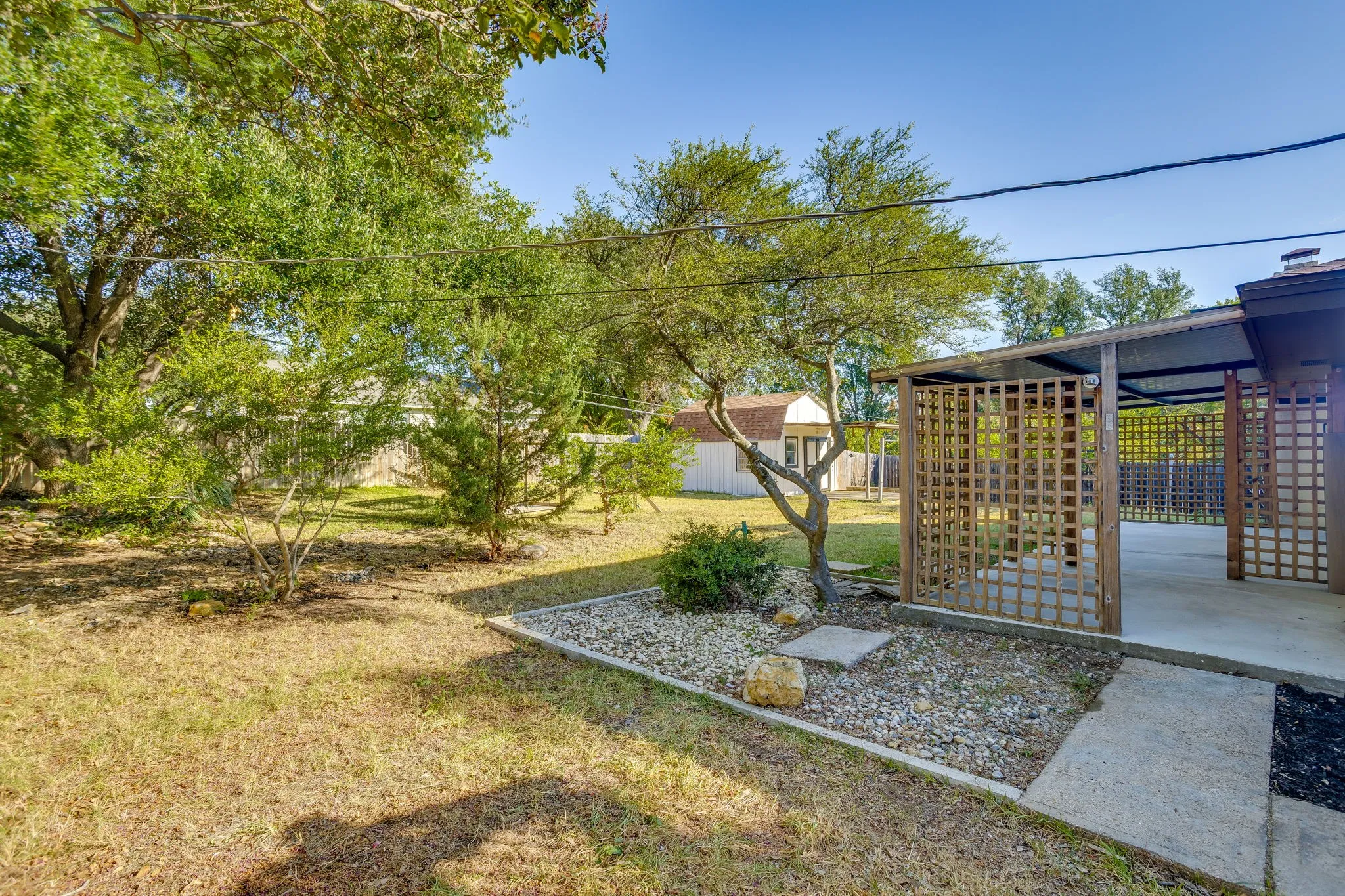 Expansive backyard with mature trees, covered patio featuring lattice privacy screens, concrete patio flooring, and a separate storage shed