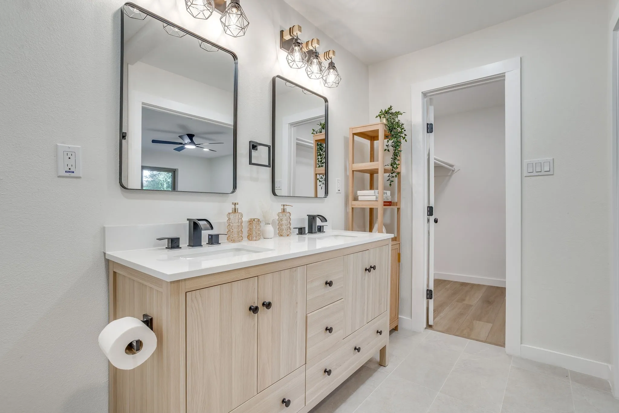 Dual vanity with a light wood-finish cabinet and white countertop, framed mirrors, matte black fixtures, and geometric light fixtures