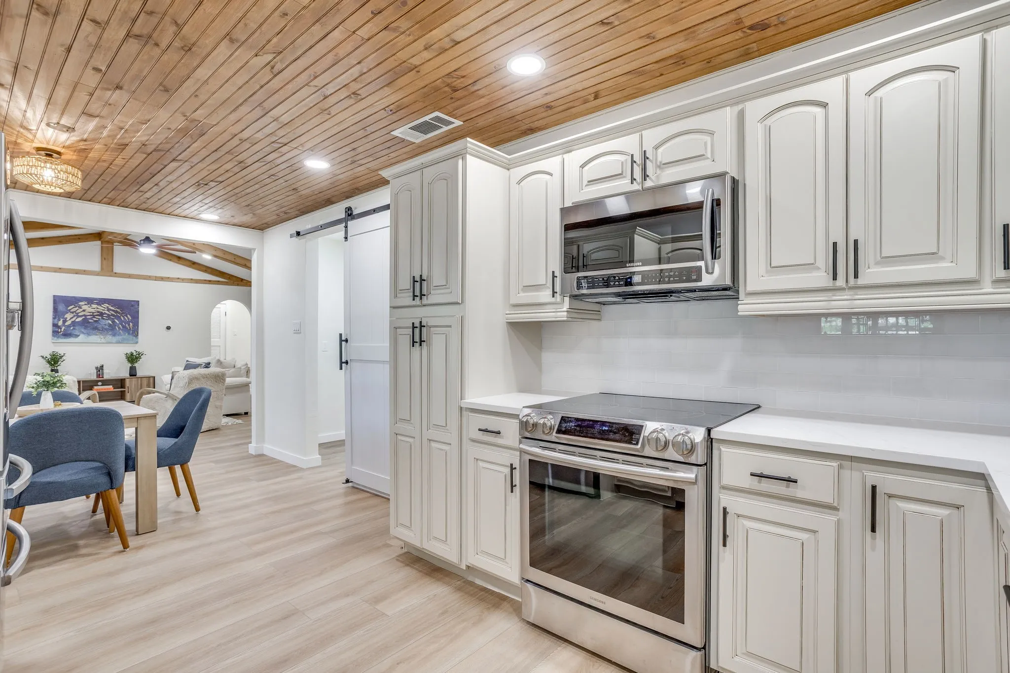 Kitchen featuring white cabinetry, stainless steel appliances, wood-finish flooring, white countertops, and a subway tile backsplash