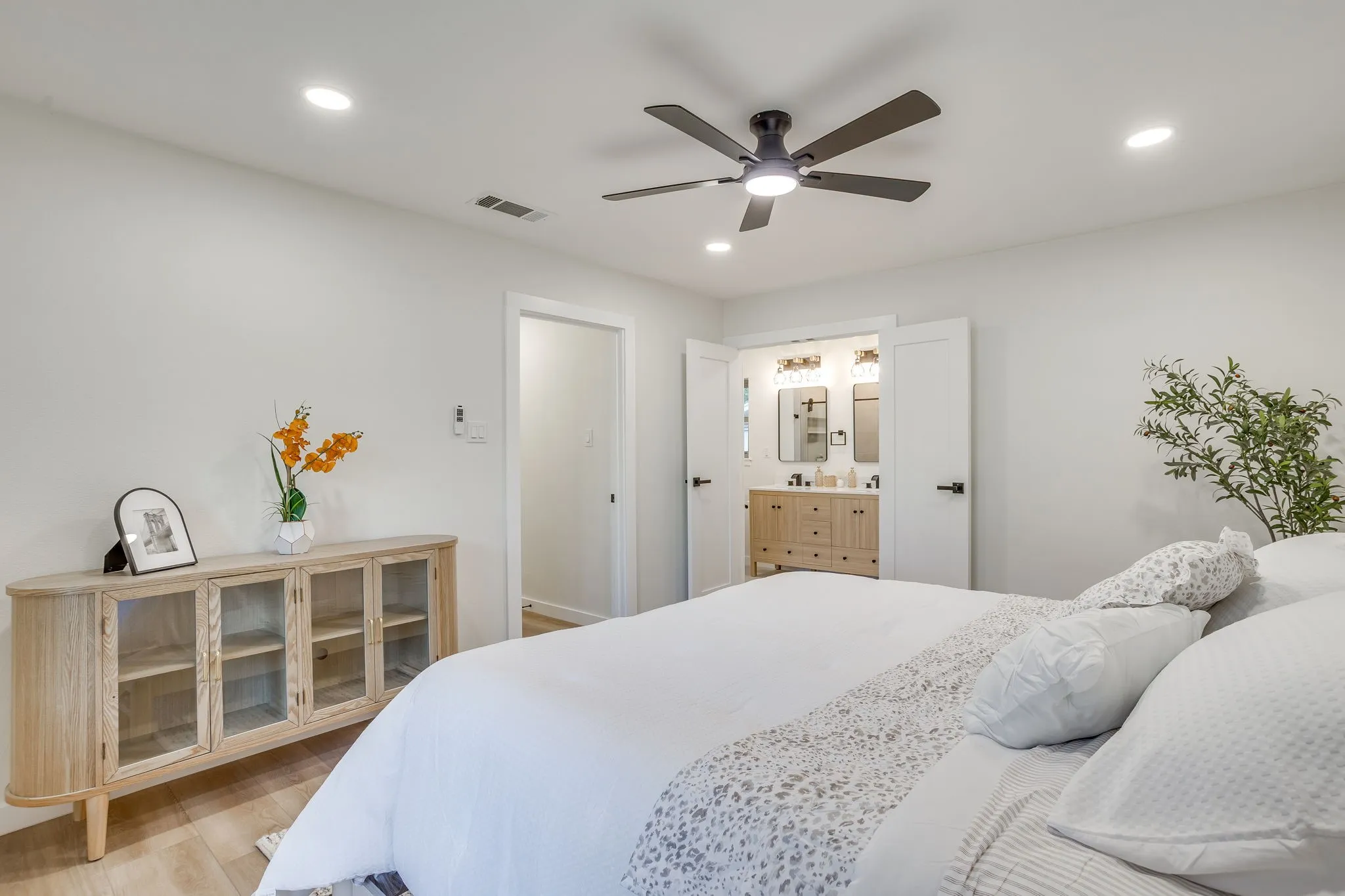 Recessed lighting, ceiling fan, wood-finish flooring, white walls, and double doors opening to a bathroom with a dual vanity