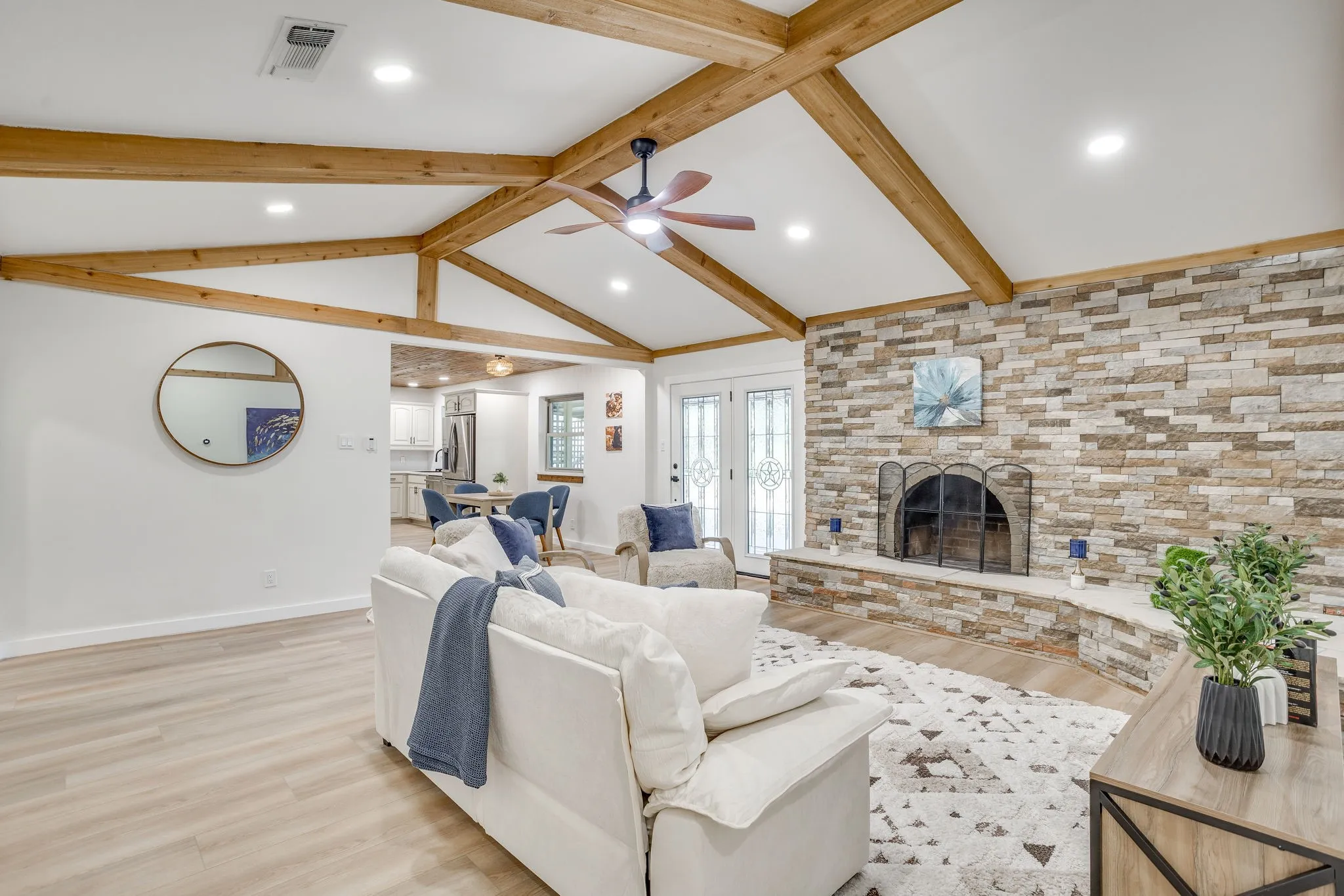Vaulted ceiling with exposed wood beams, stone-clad fireplace with hearth, recessed lighting, wood-finish flooring, and French doors