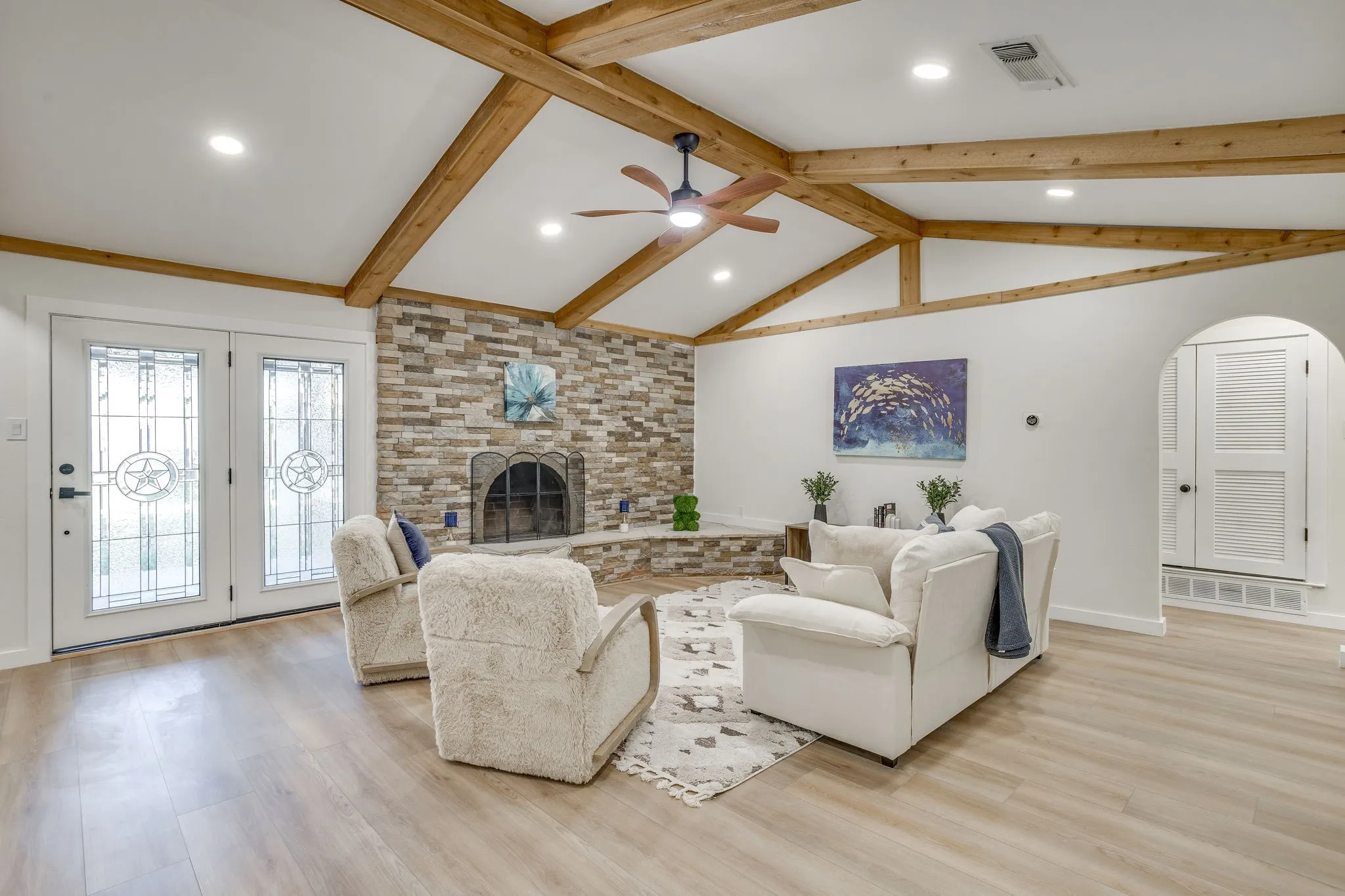 Vaulted ceiling with exposed wood beams, stone-faced fireplace, wood-finish flooring, recessed lighting, and decorative glass French doors