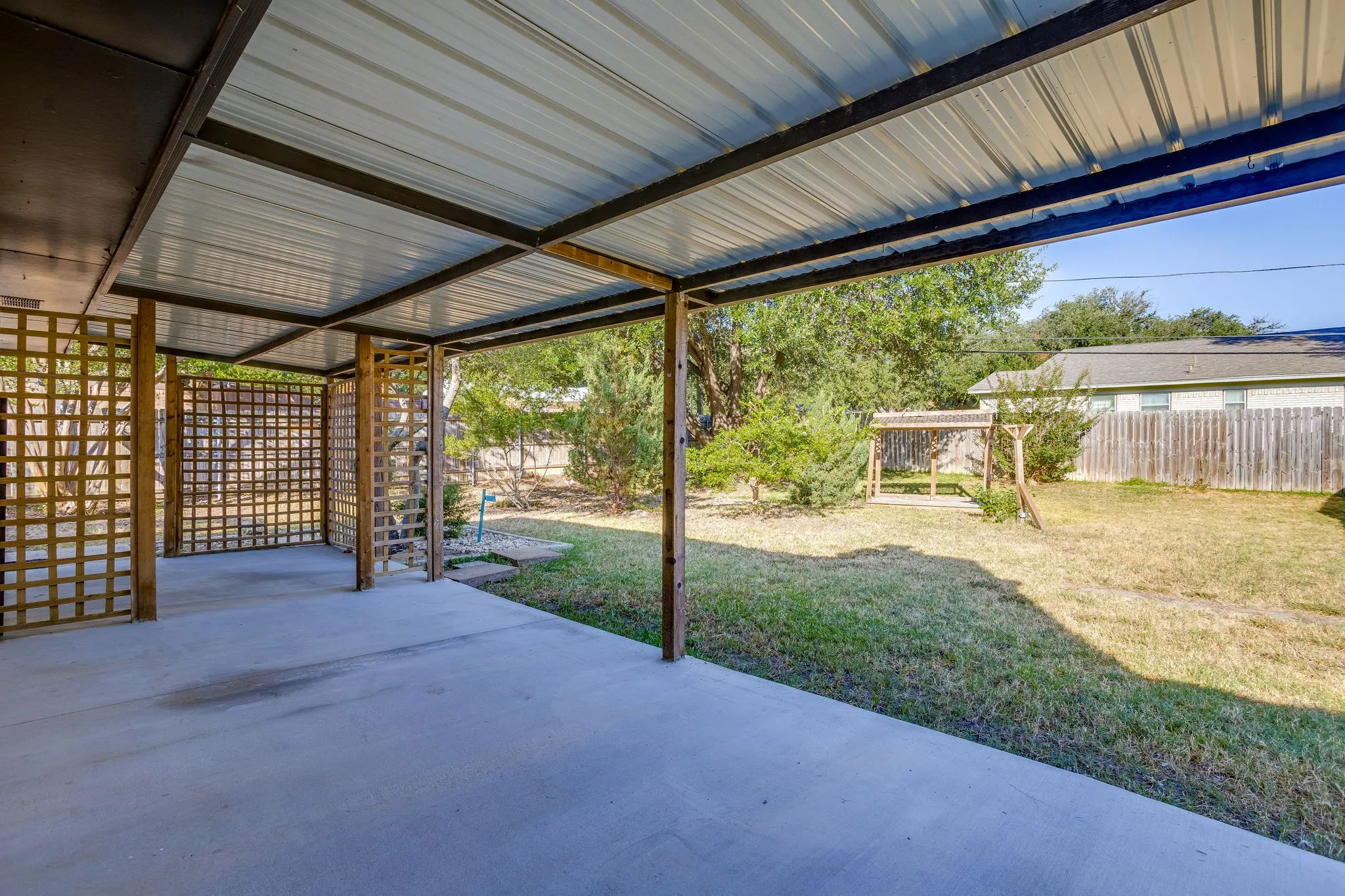 Covered patio with a corrugated metal roof, concrete flooring, and decorative lattice panels
