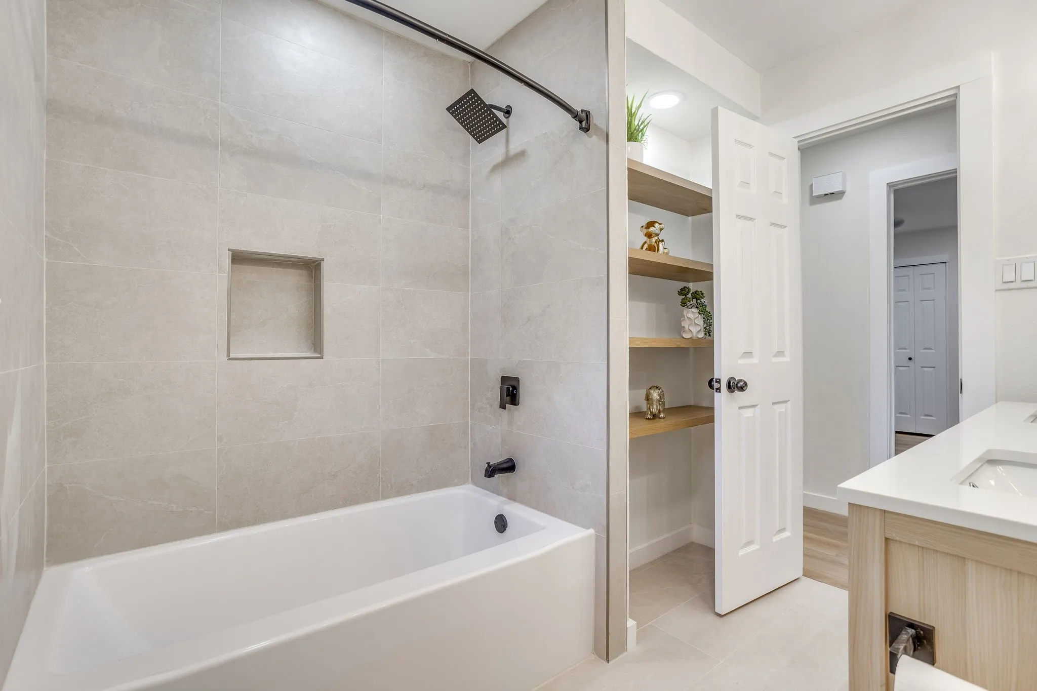 Bathtub with matte black fixtures, tiled surround, and integrated shower niche