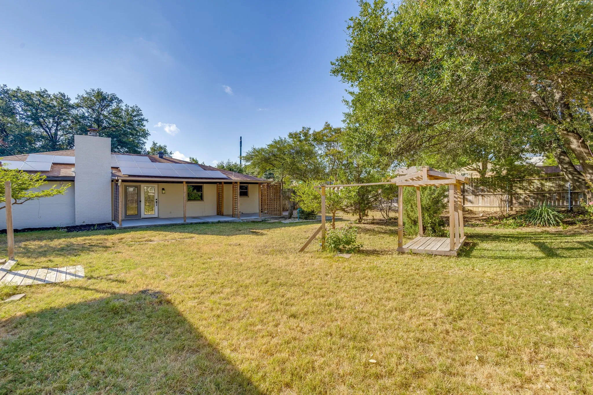 Expansive backyard with a covered patio, dual glass-paneled doors, and a wood-slat playset structure