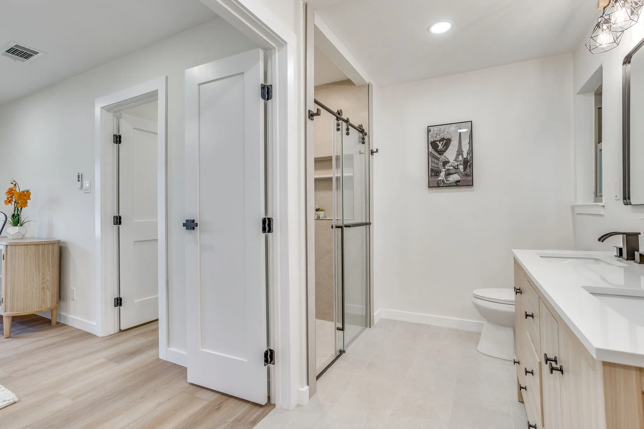 Contemporary bathroom with a dual vanity, light wood-finish cabinetry, and a walk-in shower with a sliding glass door