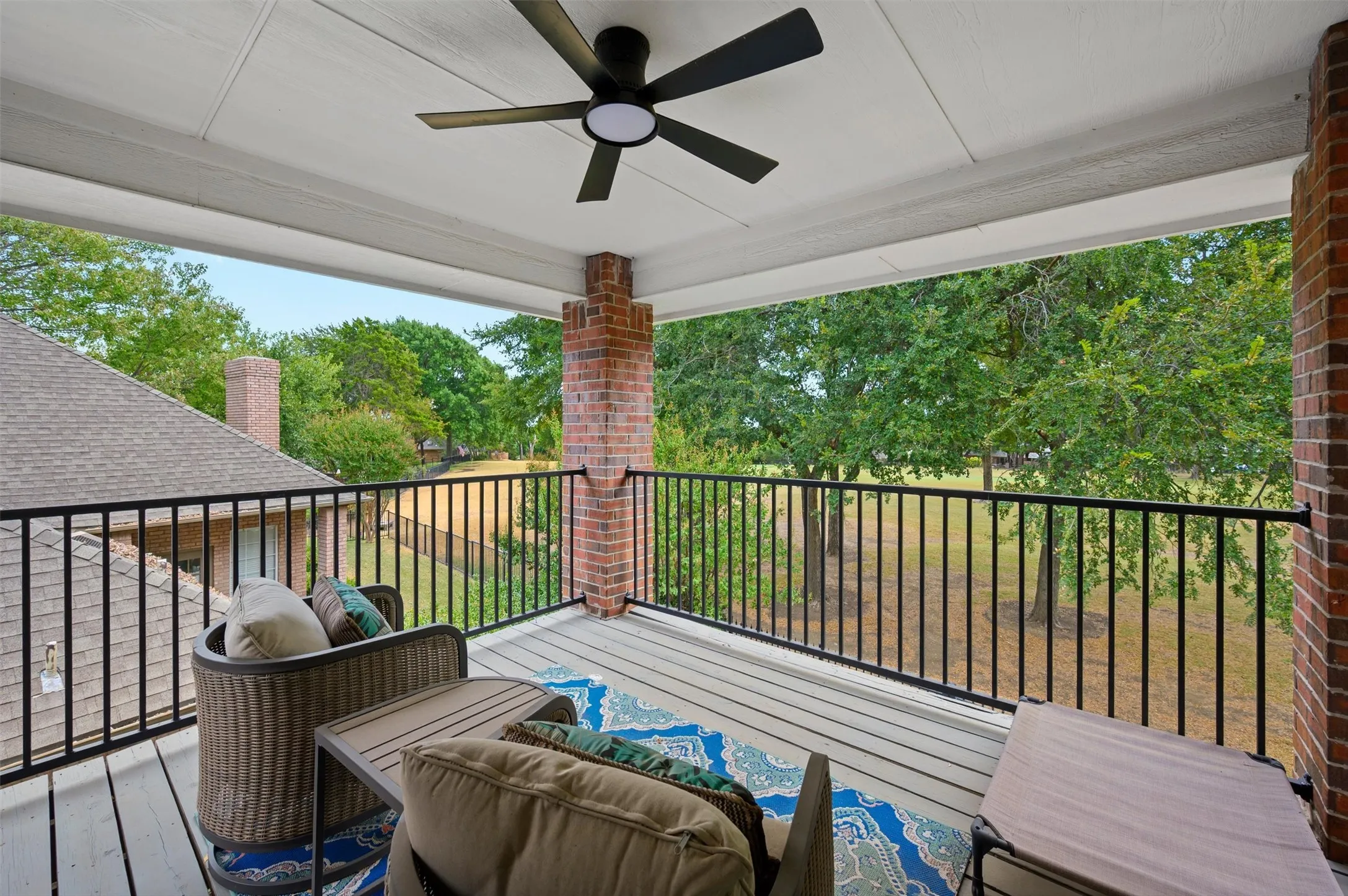 Covered outdoor balcony featuring a ceiling fan, brick column, and black metal railing
