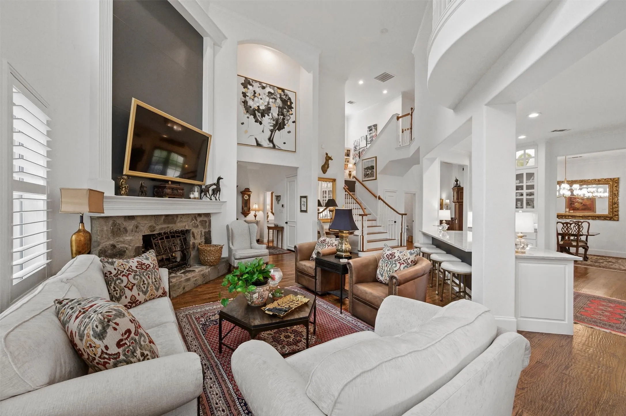 Spacious living area featuring a stone fireplace, wood-finish flooring, and high ceilings
