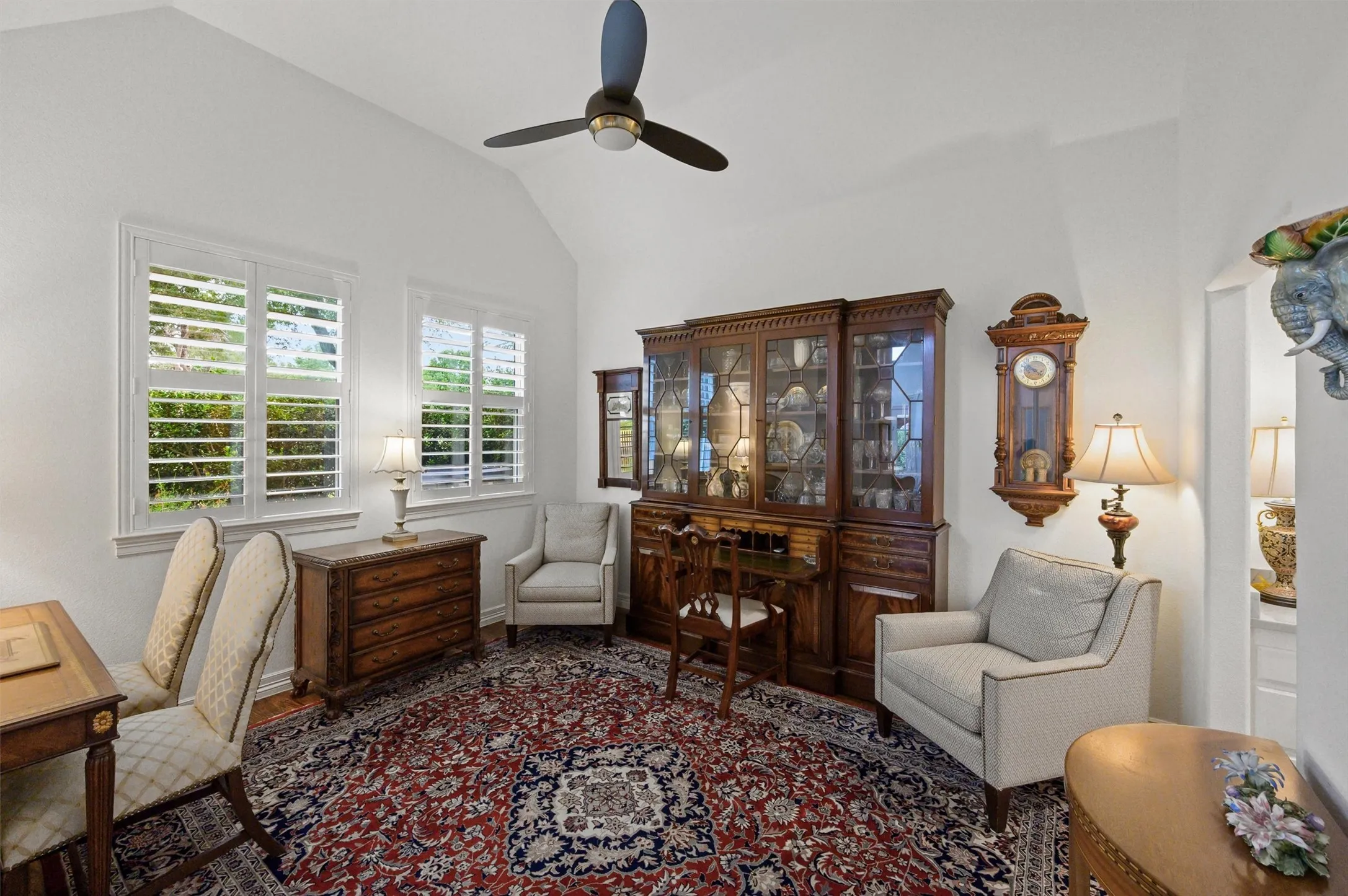 Vaulted ceiling with a ceiling fan, white plantation shutters, and wood-finish flooring