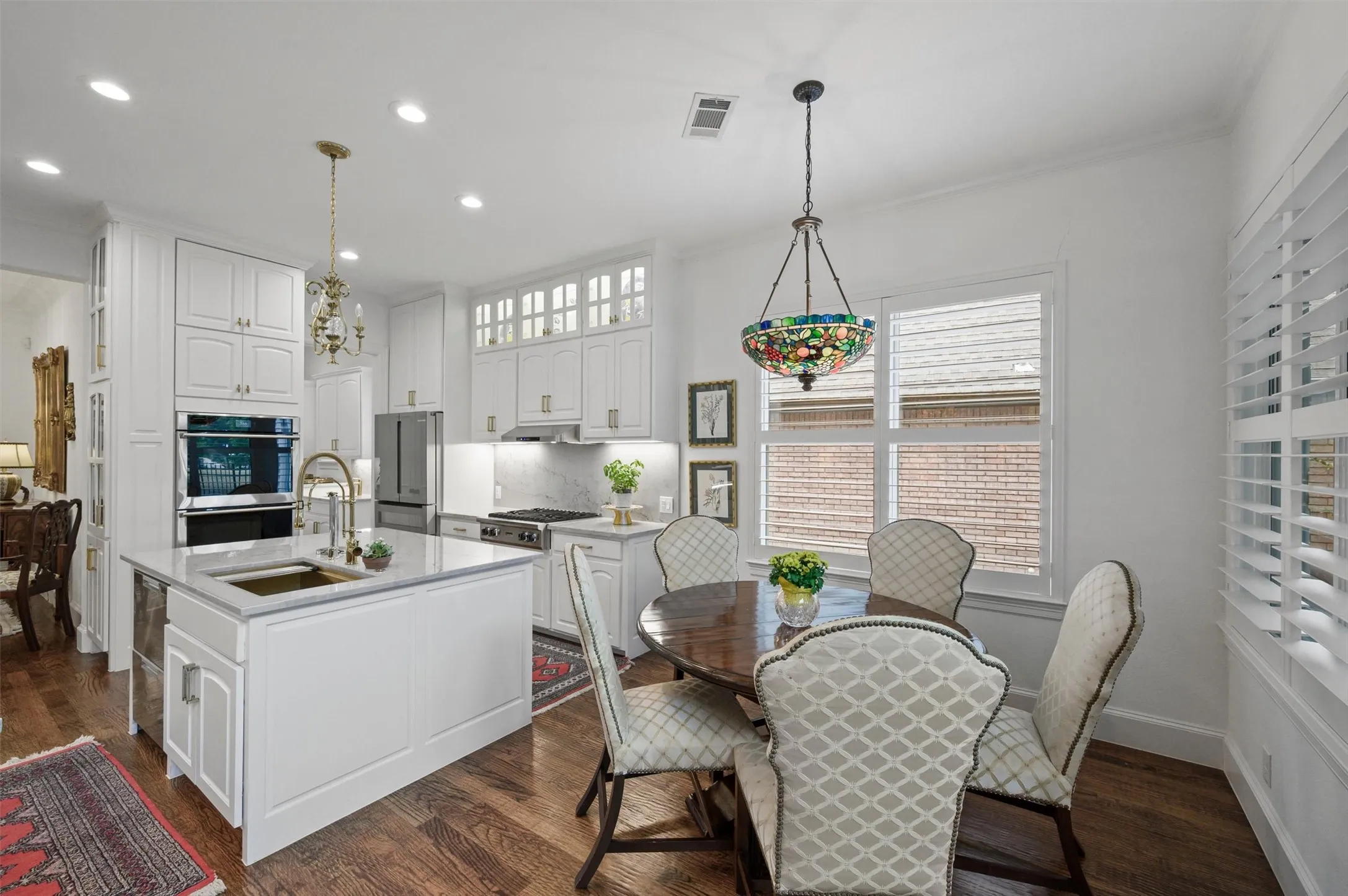 Gourmet kitchen with white cabinetry, stainless steel appliances, central island with sink, stone countertops, and wood-finish flooring