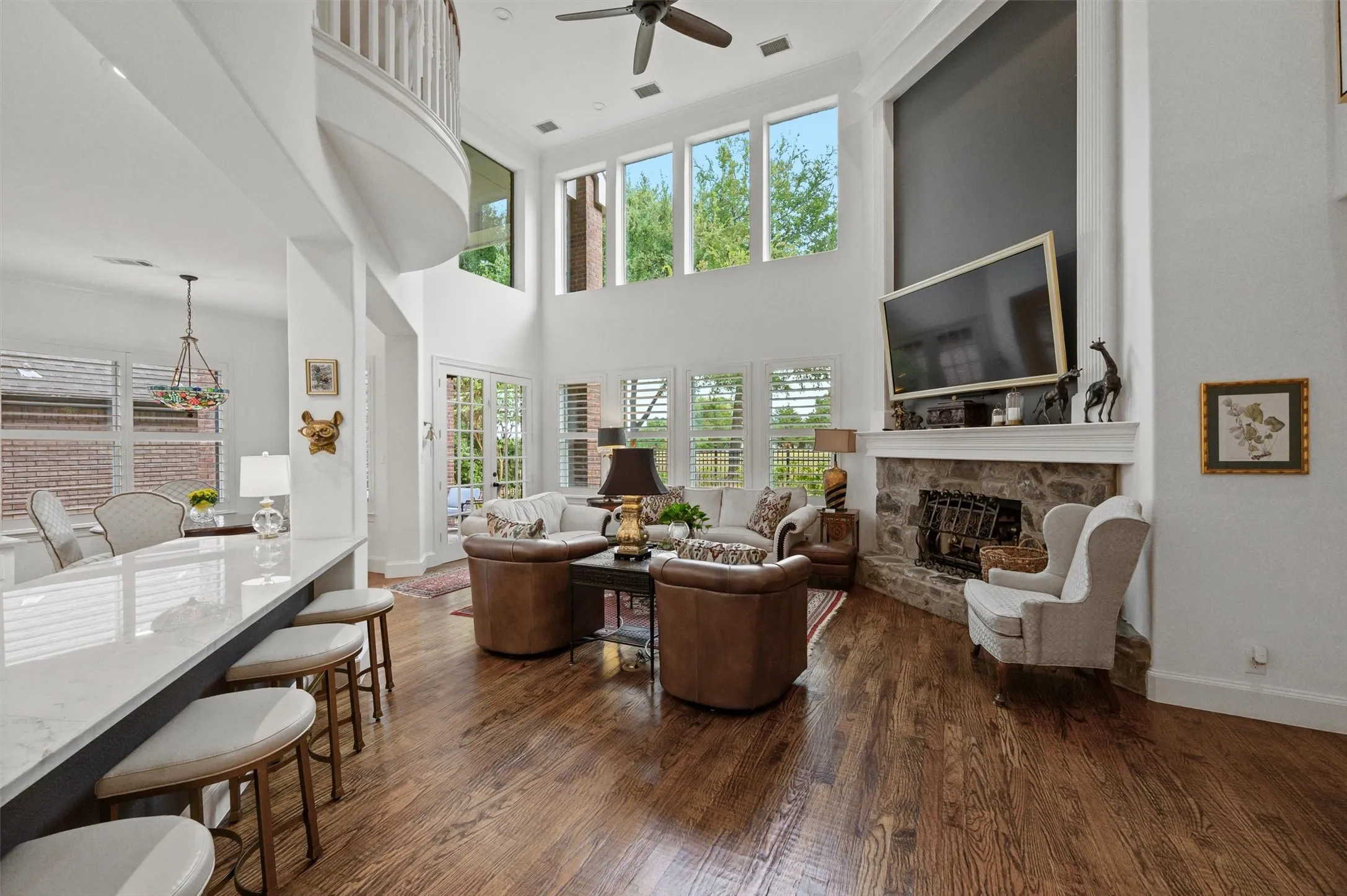 Two-story living area with high ceilings, wood-finish flooring, a stone fireplace, and multiple windows