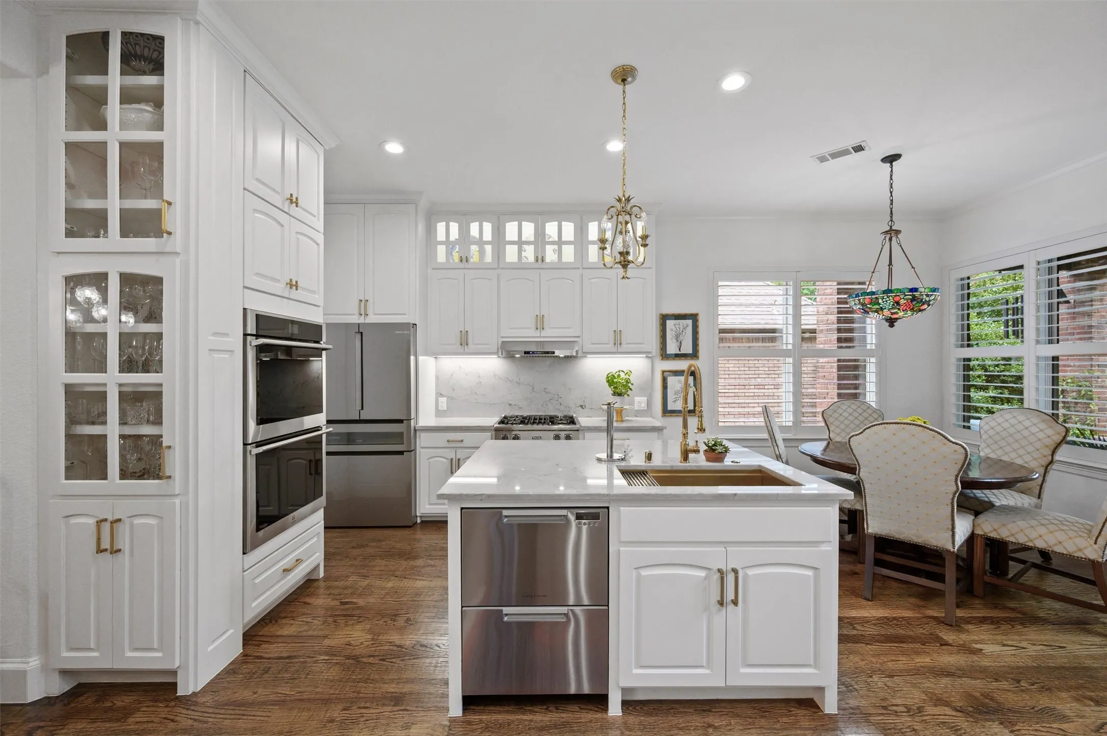 White cabinetry, stainless steel appliances, built-in double ovens, wood-finish flooring, and a center island with sink