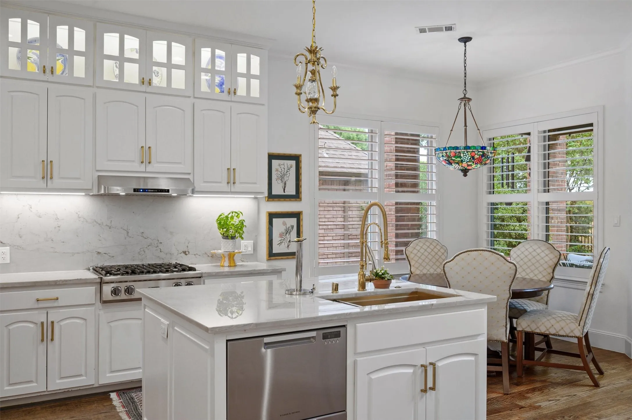 Kitchen featuring white cabinetry, a gas range, a central island with an undermount sink, and plantation shutters