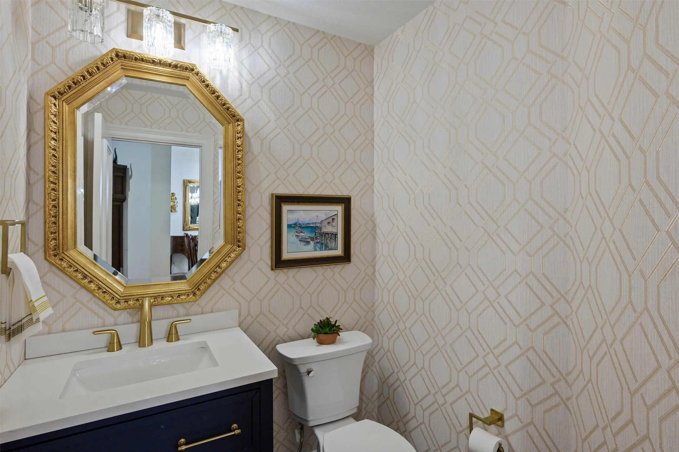Powder room with geometric pattern wallpaper, a gold-framed octagonal mirror, a vanity with a white countertop, and gold-finish hardware