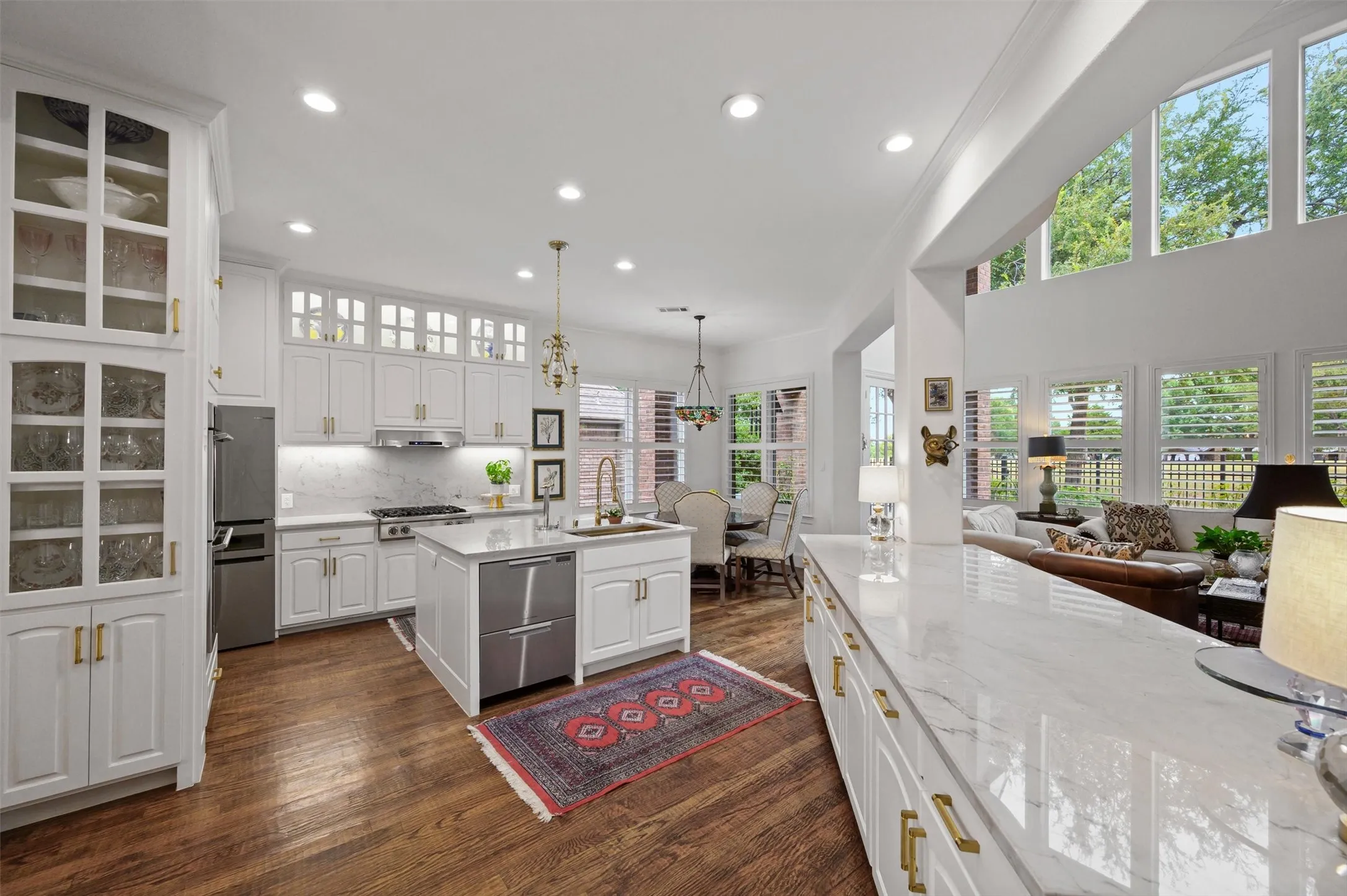 Spacious kitchen with wood-finish flooring, white cabinetry, integrated stainless steel appliances, and a central island with a built-in sink