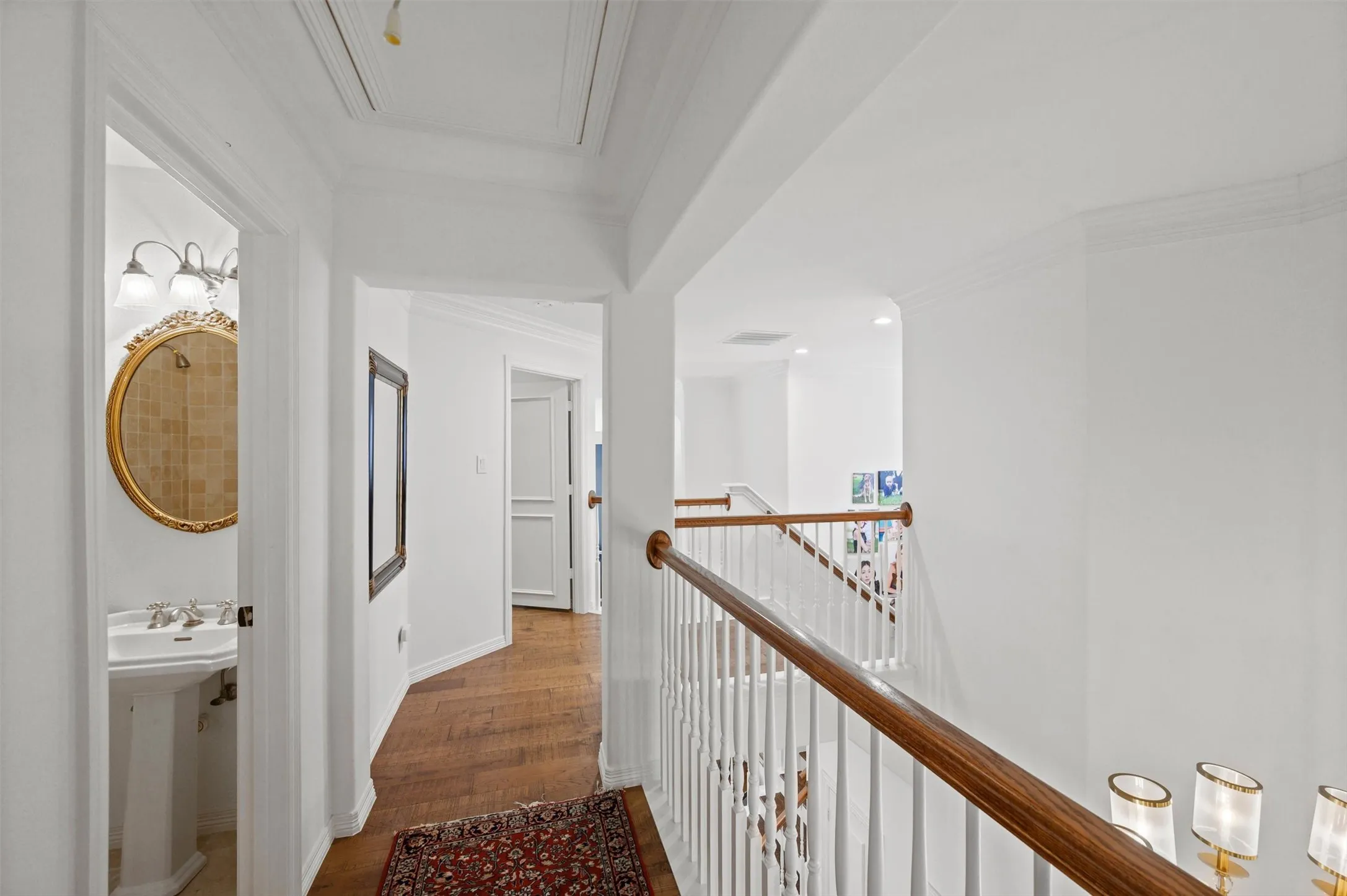 Hardwood flooring, white painted walls, white spindle staircase with wood handrail, crown molding, and recessed lighting