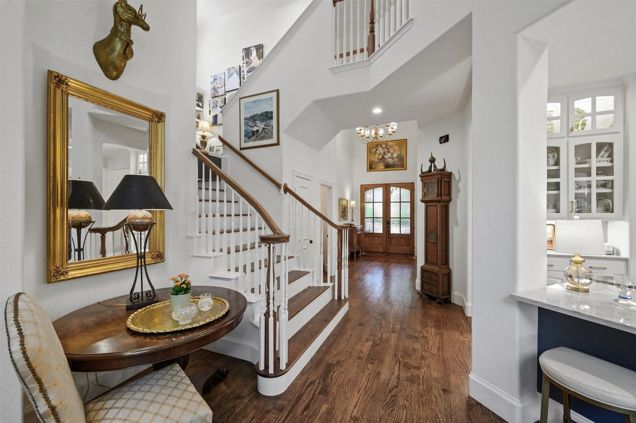 Hardwood flooring throughout, a grand staircase with wood handrails, and a two-story entryway featuring double wood-paneled doors