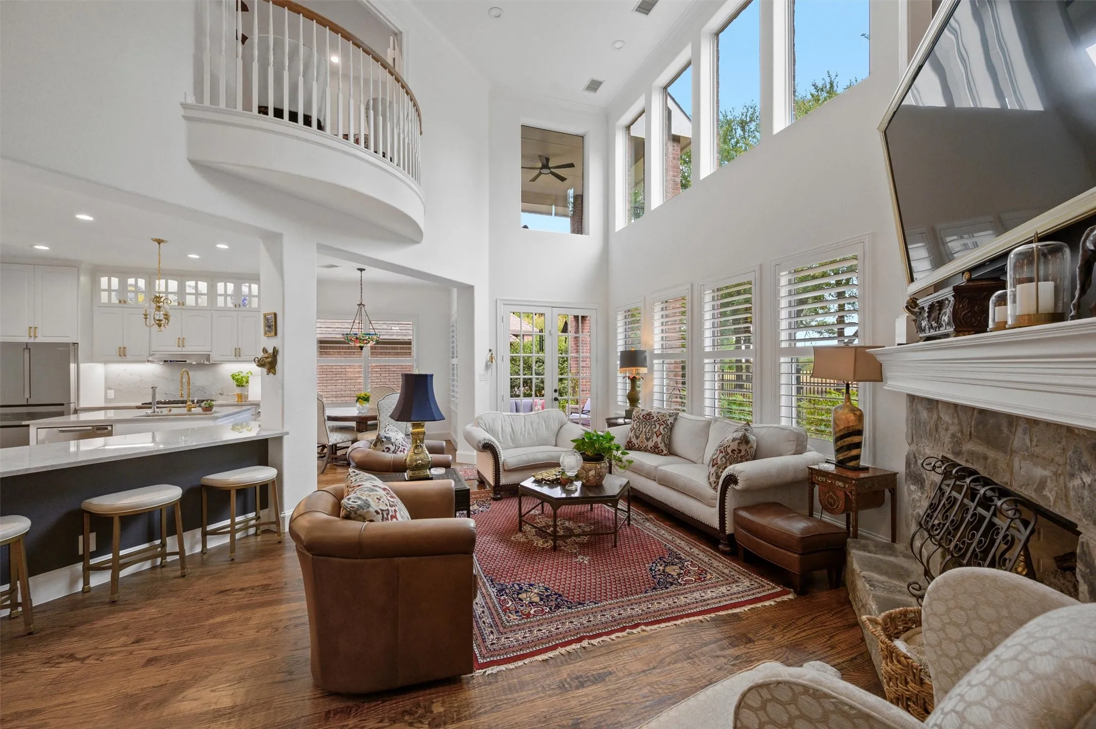 Two-story living area with high ceilings, upper-level balcony, and wood-finish flooring
