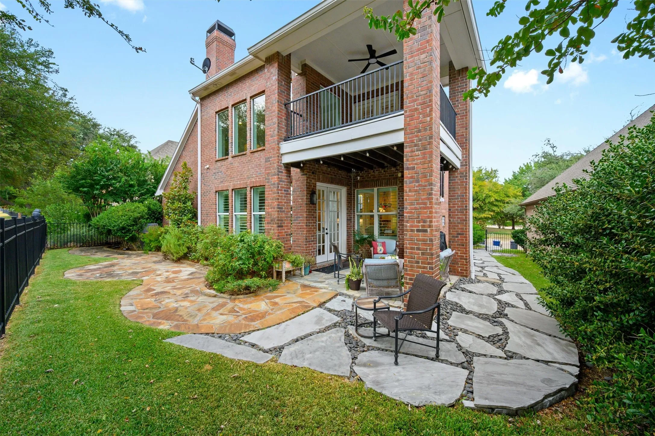 Brick exterior with multiple windows, second-story balcony, covered patio, and flagstone pathways