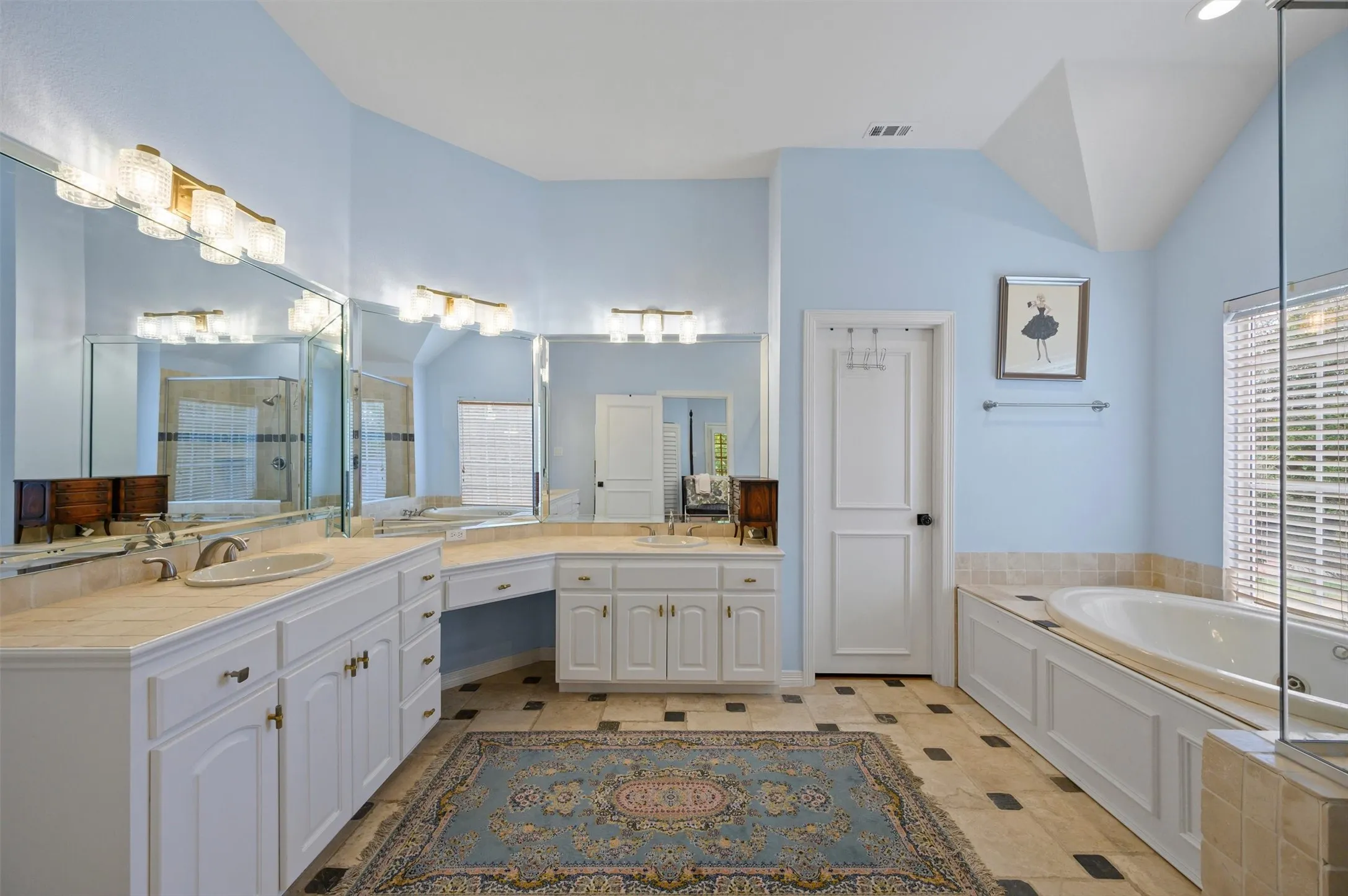Dual vanity with integrated sinks, built-in vanity seating, vaulted ceiling, tile flooring, and a separate soaking tub