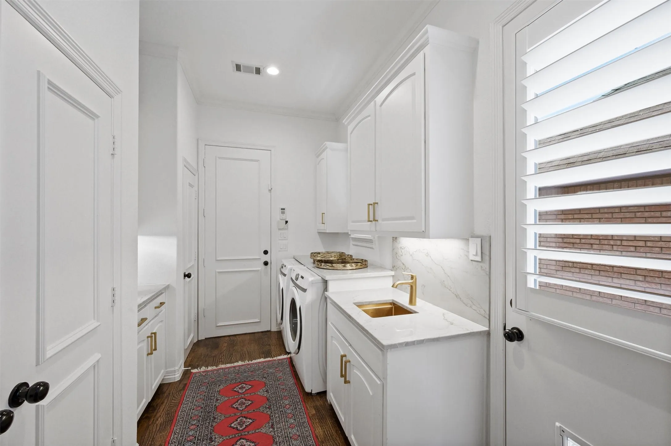 Laundry area featuring white cabinetry, a gold-toned sink, stone-finish countertops, and plantation shutters
