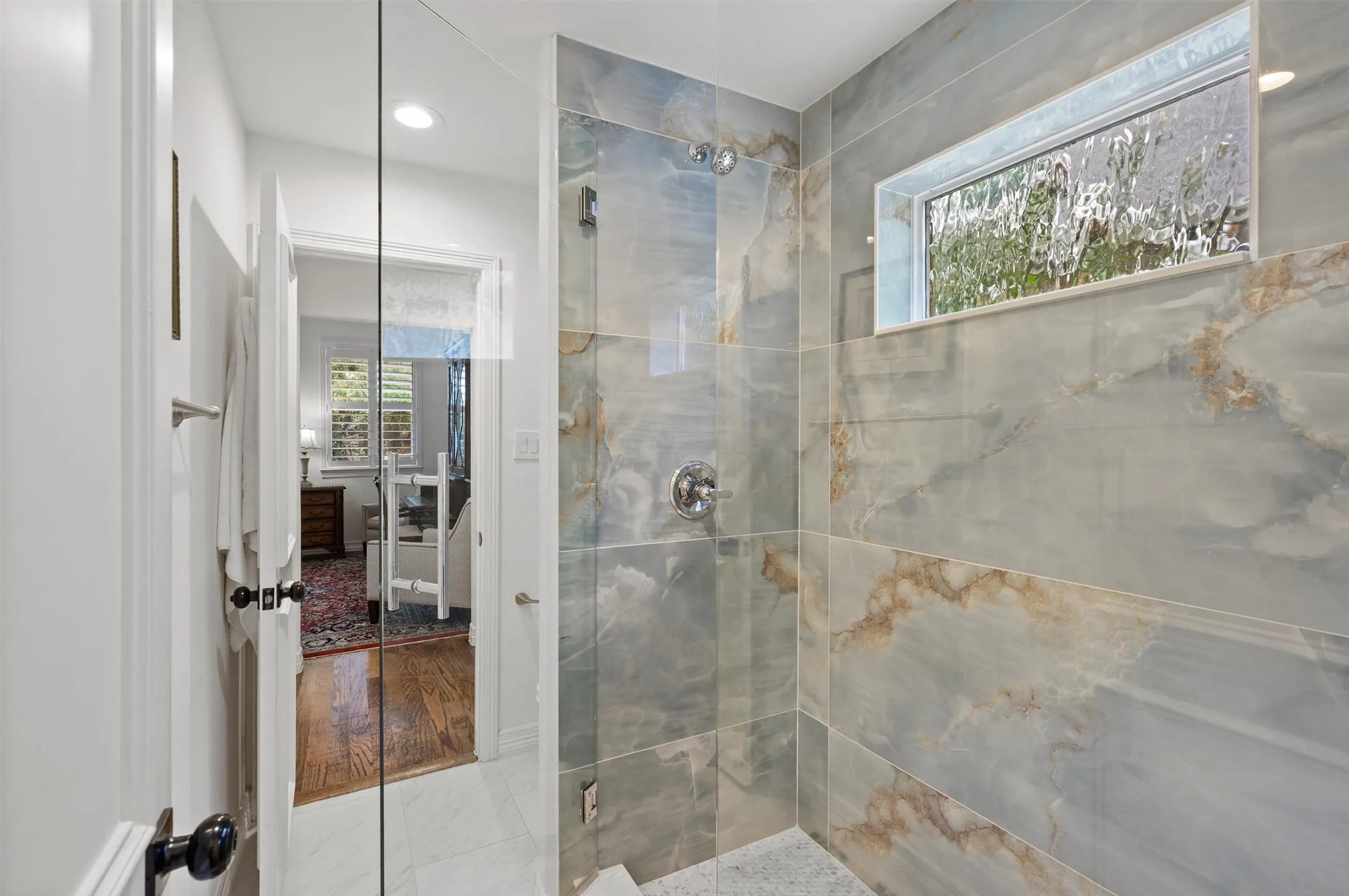 Glass-enclosed shower with large format wall tiles, a rainfall showerhead, and a textured privacy window