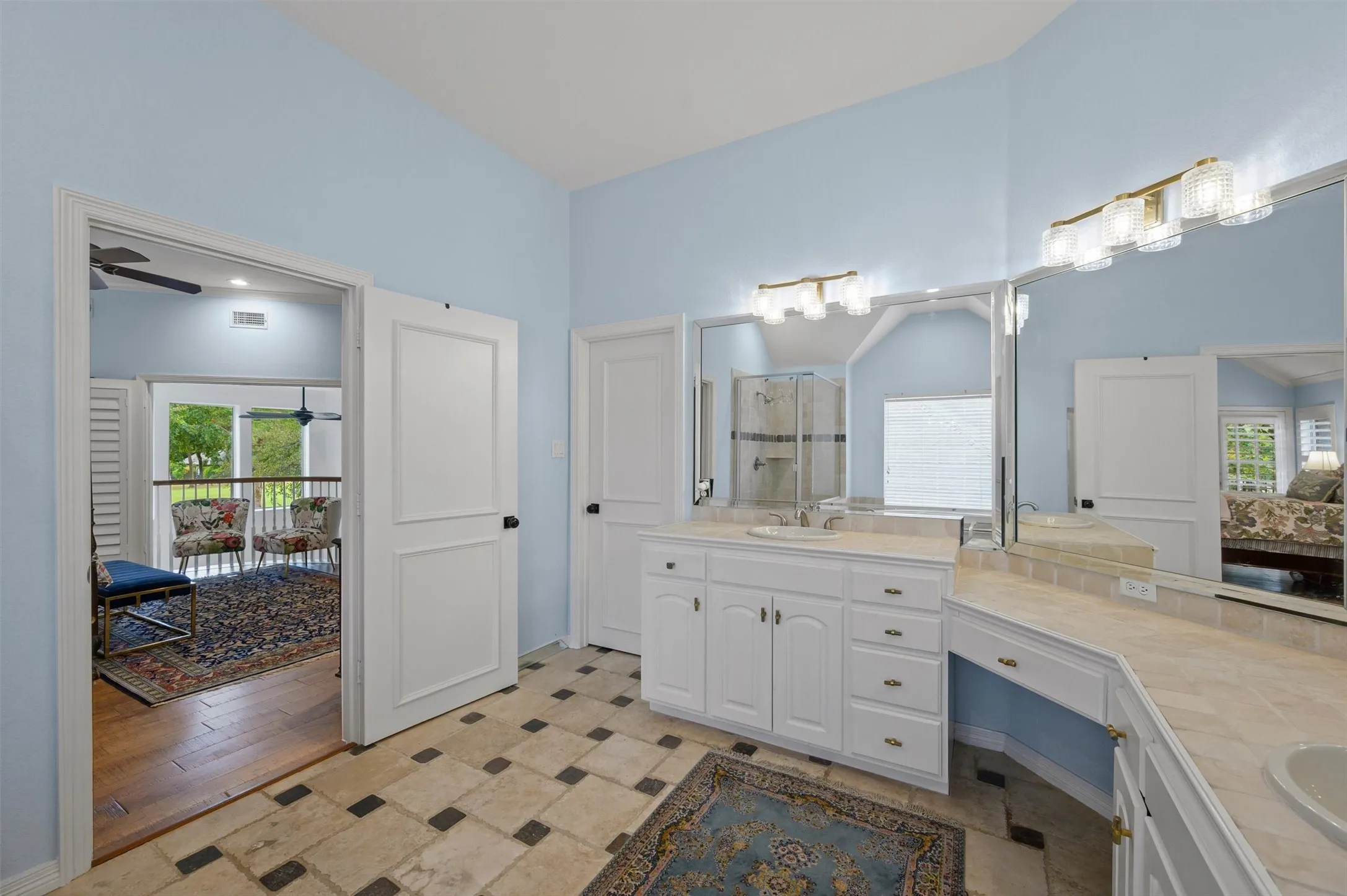 Spacious bathroom featuring a dual vanity, built-in cabinetry, and tile flooring, with an adjacent room offering access to an outdoor balcony