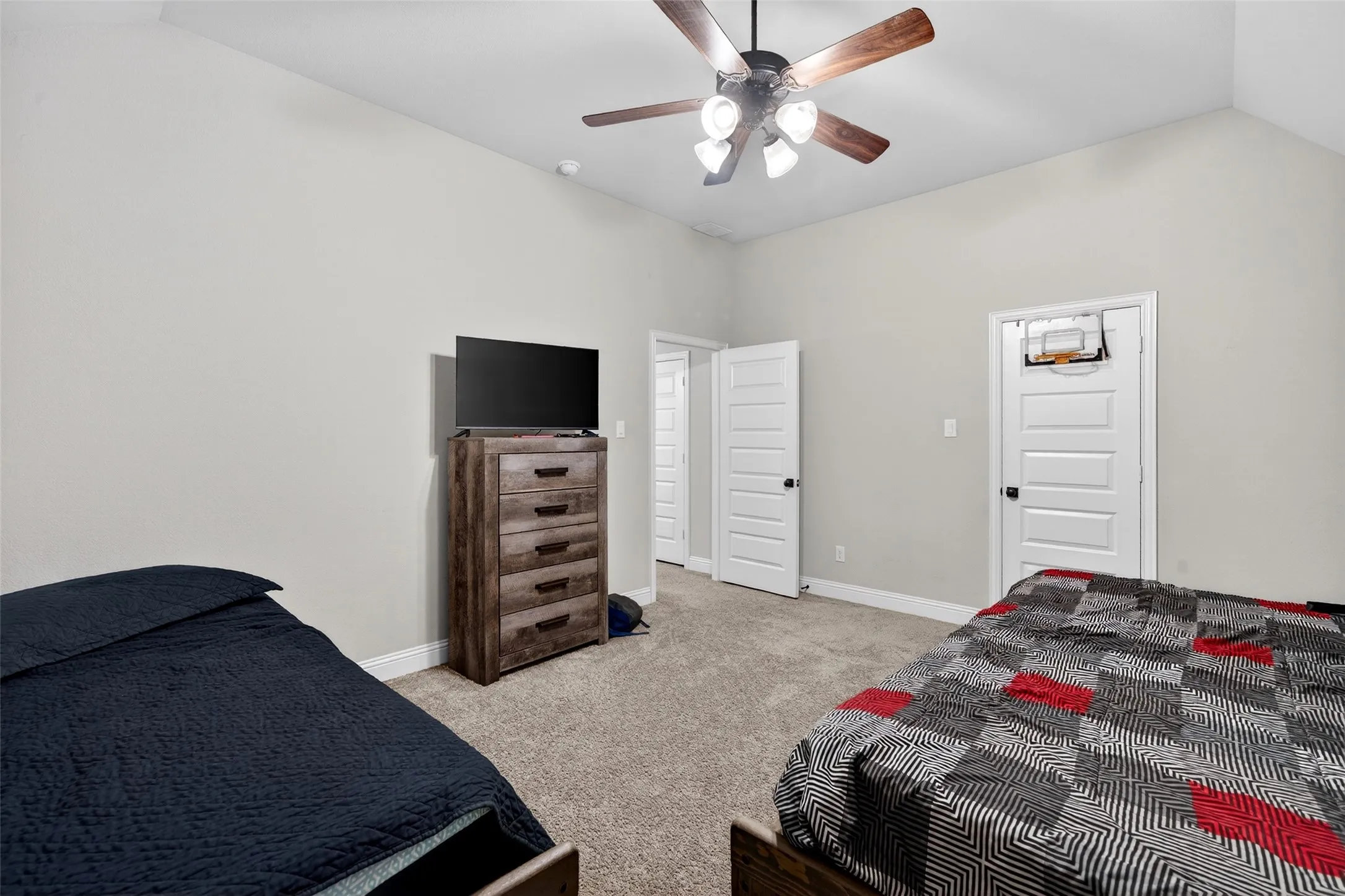 Vaulted ceiling with a wood-finish ceiling fan, neutral wall paint, and plush carpeting