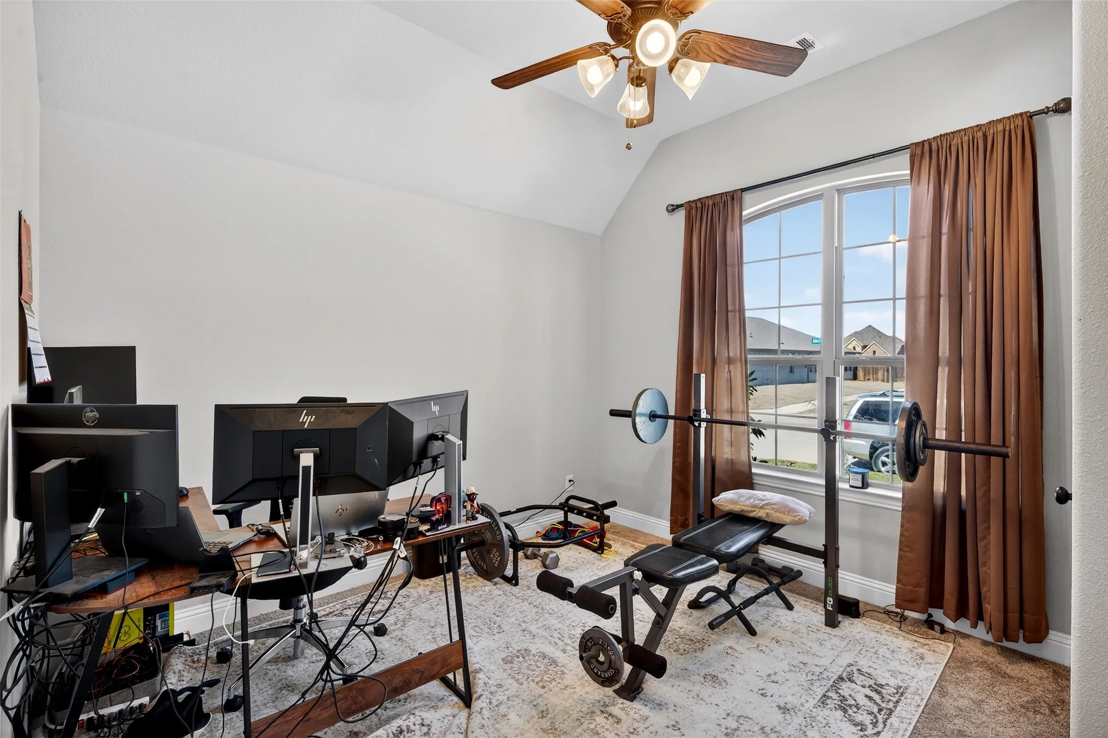 Vaulted ceiling with an illuminated ceiling fan, arched window with a grid pattern, and neutral wall tones