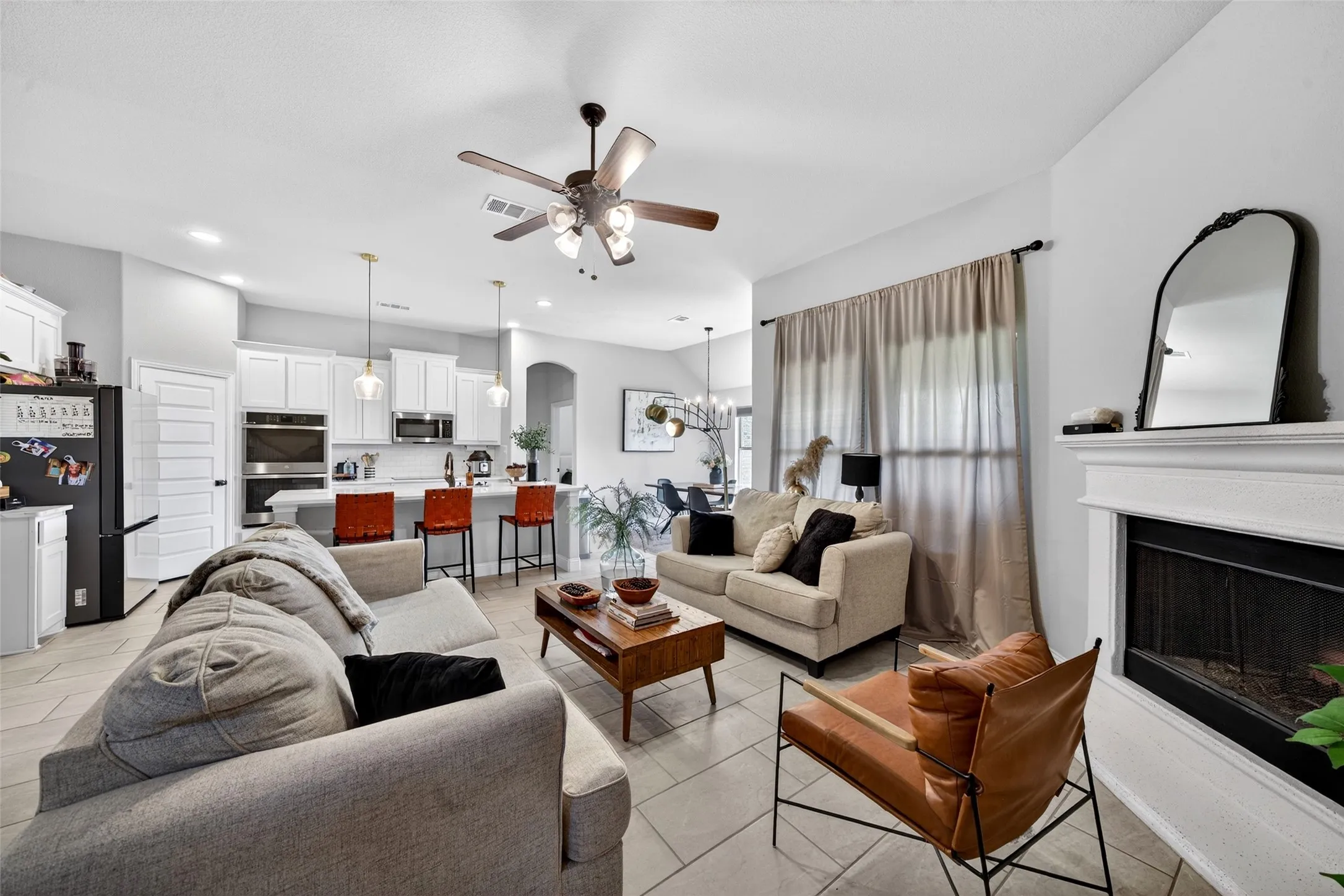 Open-concept living space featuring a fireplace with a white mantel, tiled flooring, and a ceiling fan