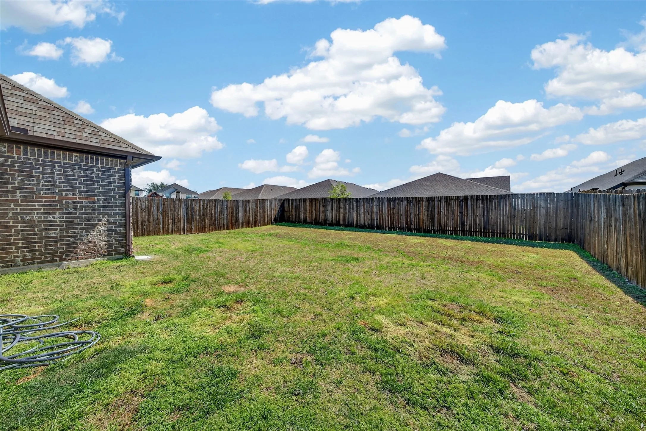 Expansive grassed area with full perimeter wood fencing and a brick-faced exterior wall
