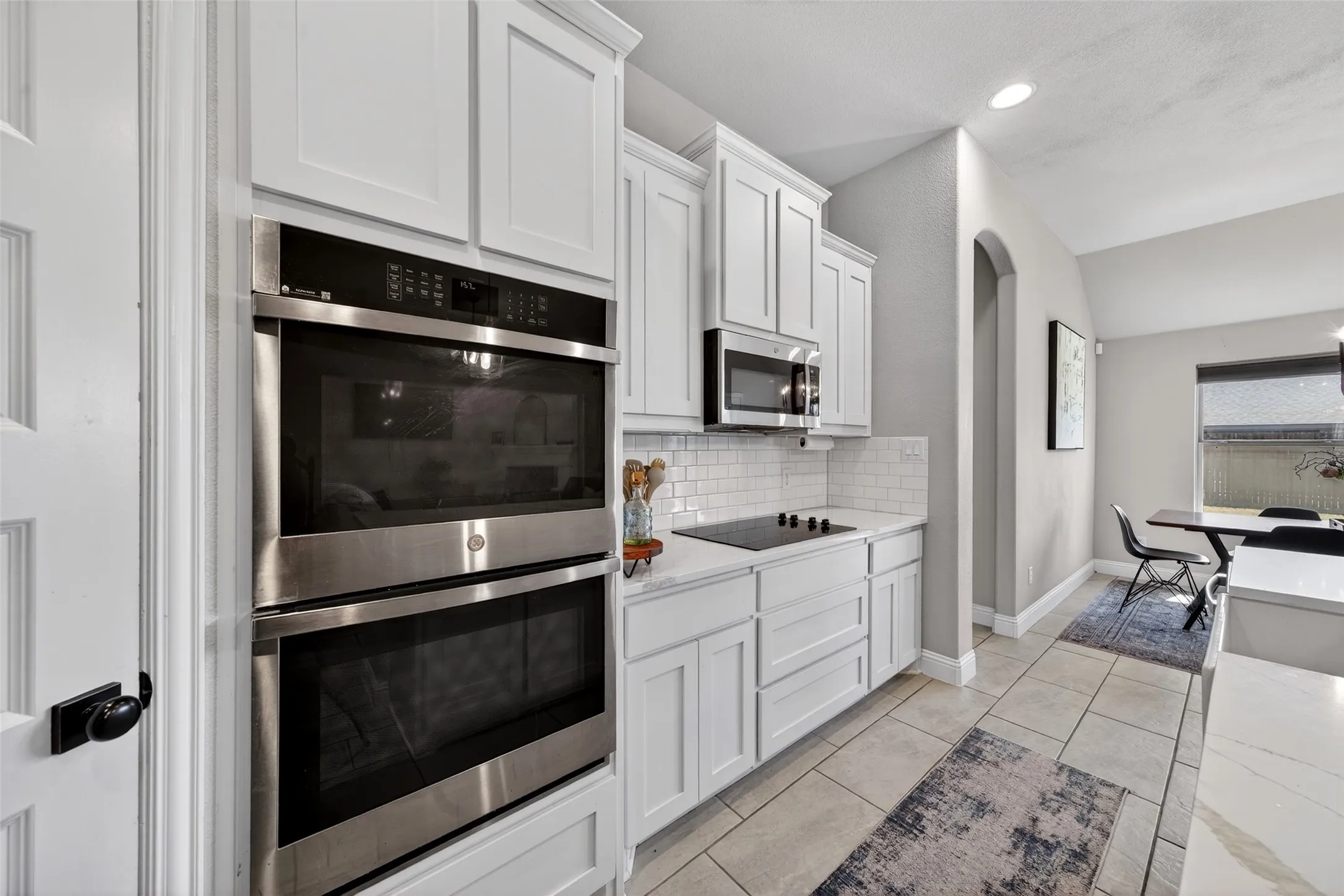 Kitchen featuring white shaker cabinetry, stainless steel double ovens, stainless steel microwave, cooktop, and subway tile backsplash