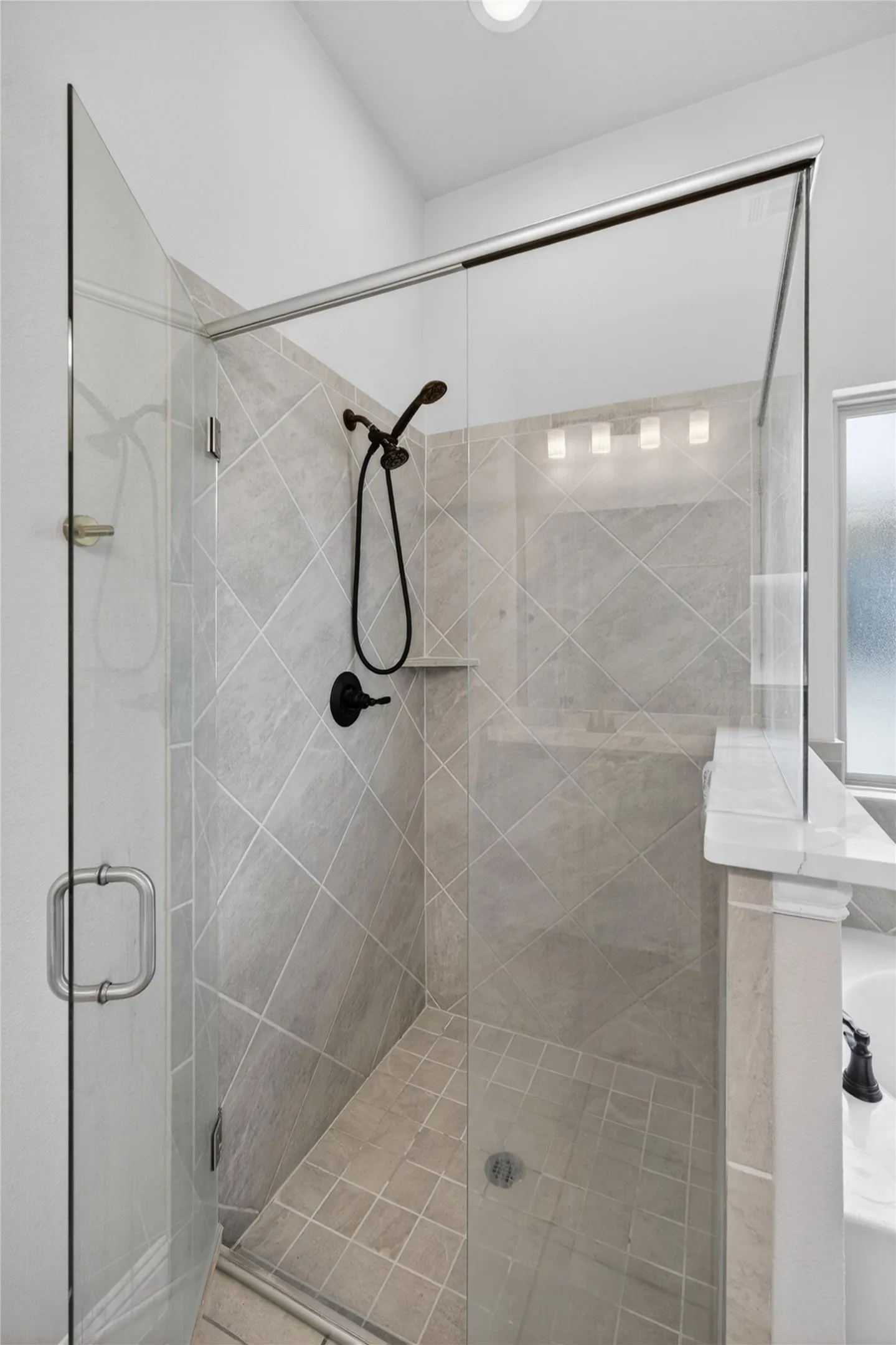 Glass-enclosed shower featuring diagonal tile work, matte black fixtures, an integrated shower niche, and a tiled shower pan