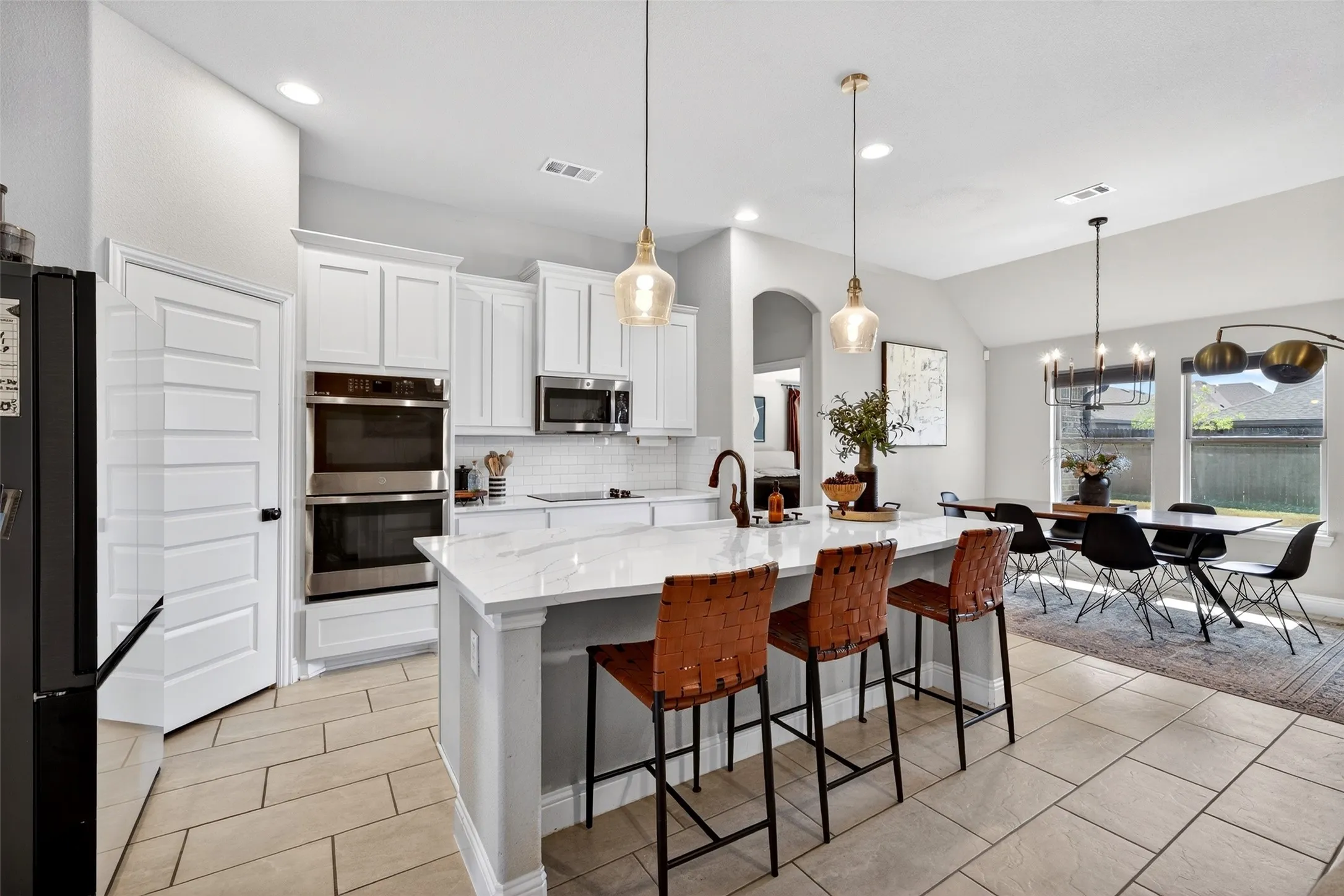 Kitchen featuring a large island with a countertop, white cabinetry, stainless steel double ovens, and tile flooring