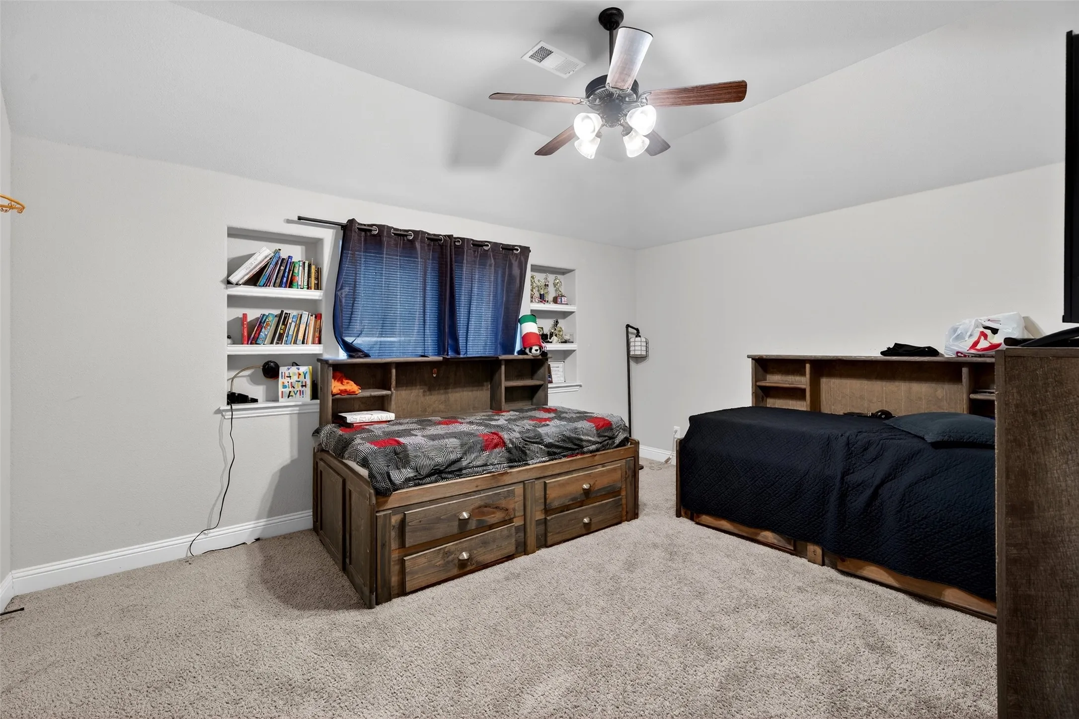Carpeted room featuring a ceiling fan, recessed wall shelving, and neutral wall paint